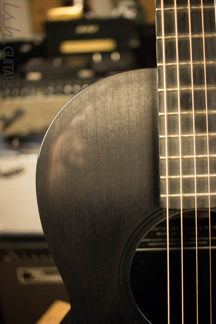 A black acoustic guitar with a blurred out soundboard in the background. - Guitar