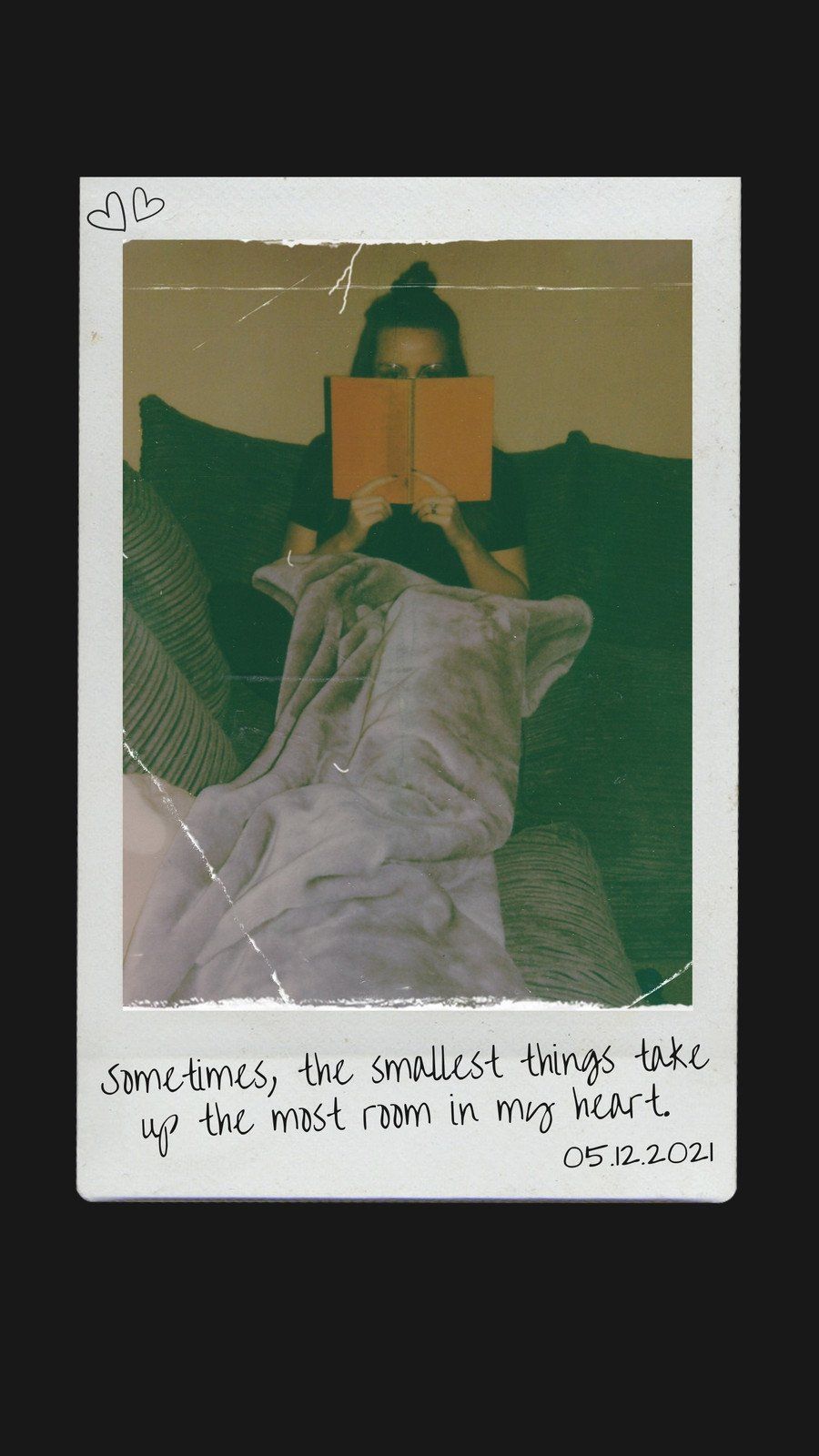 Polaroid of a woman lying on a couch reading a book. The polaroid has a caption that says 