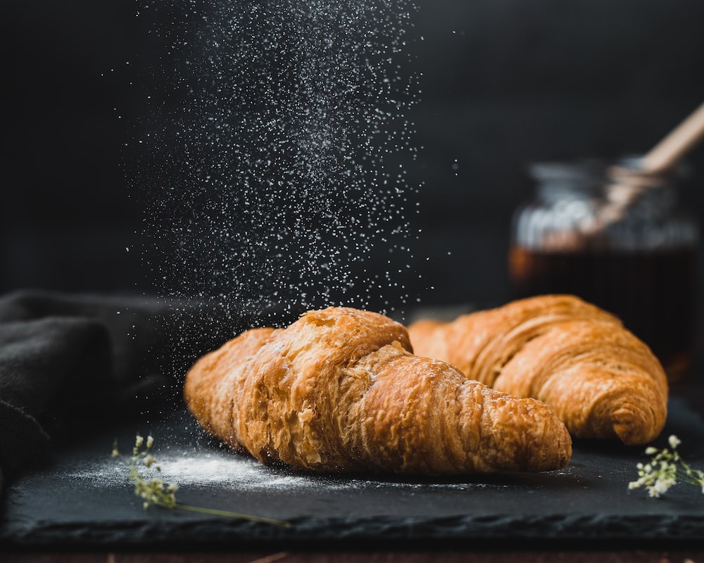 Two croissants on a black slate with powdered sugar - Bakery