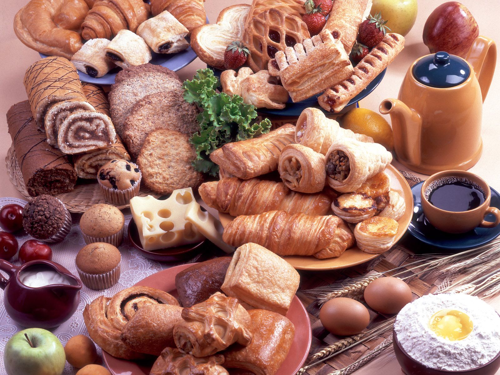 A table full of different types of bread, pastries, eggs, cheese, and coffee. - Bakery