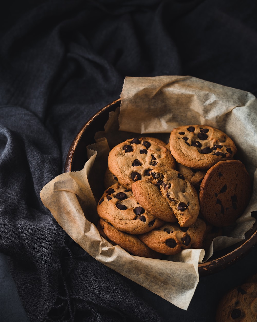 A basket of chocolate chip cookies on a black cloth. - Bakery
