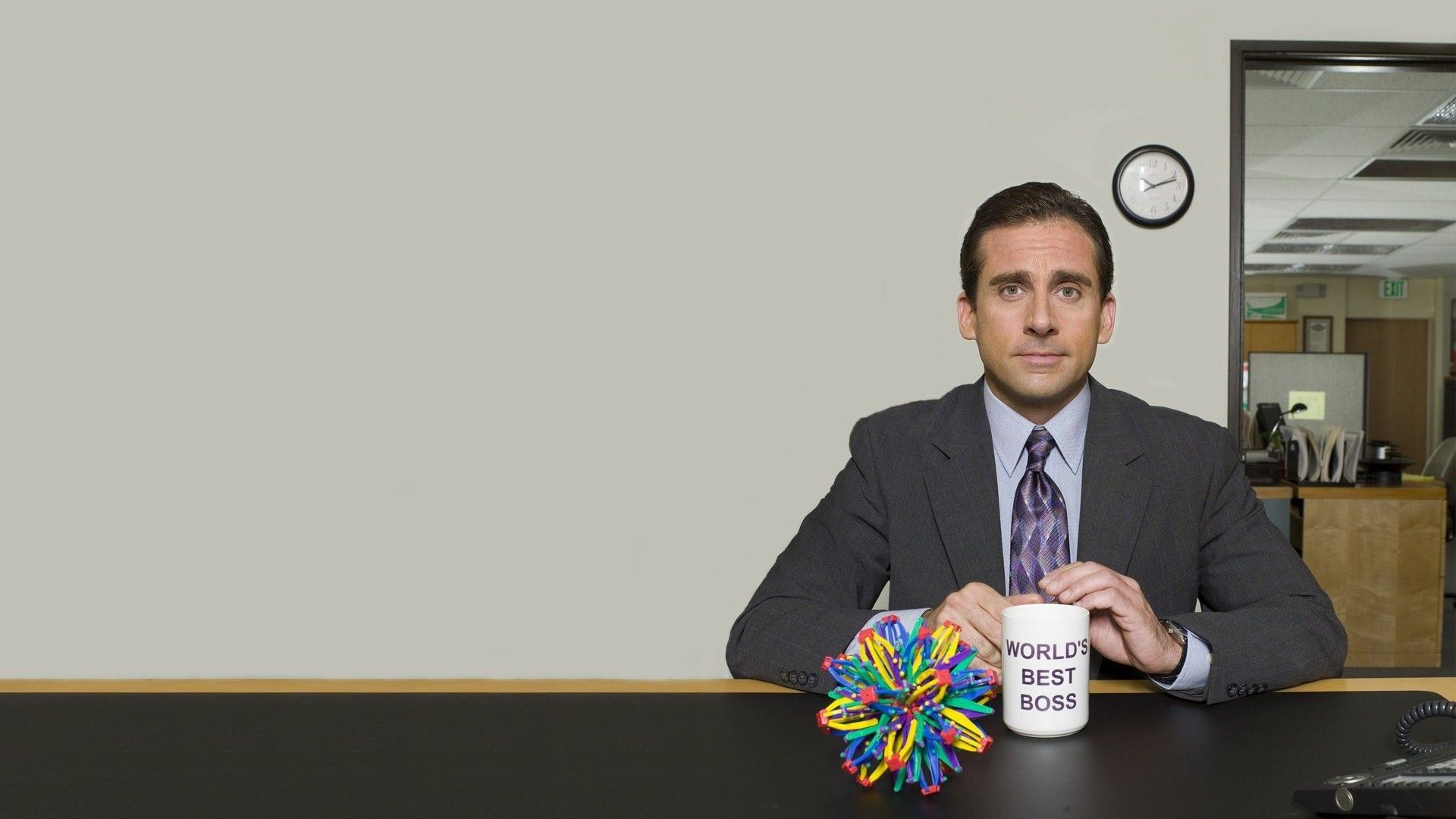 Michael Scott sitting at a desk with a coffee mug that says 