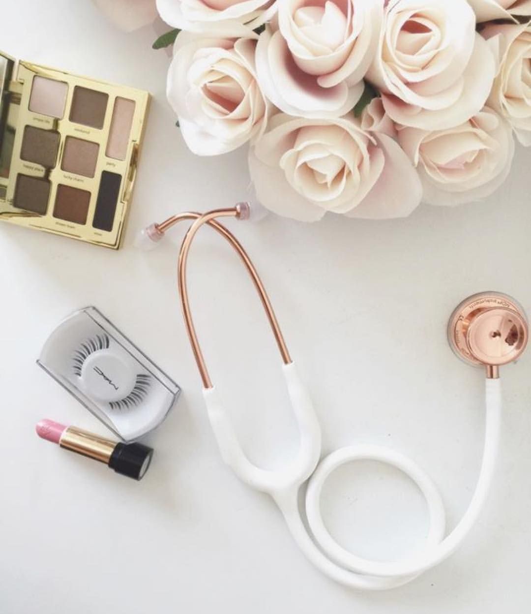 A rose gold stethoscope surrounded by makeup and flowers - Nurse