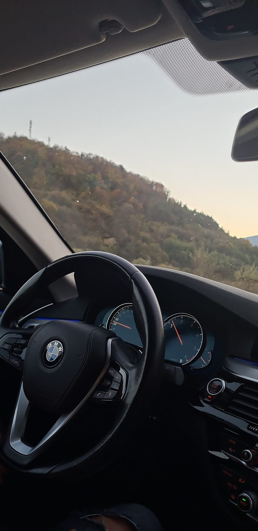 A car dashboard with a hill in the background. - BMW