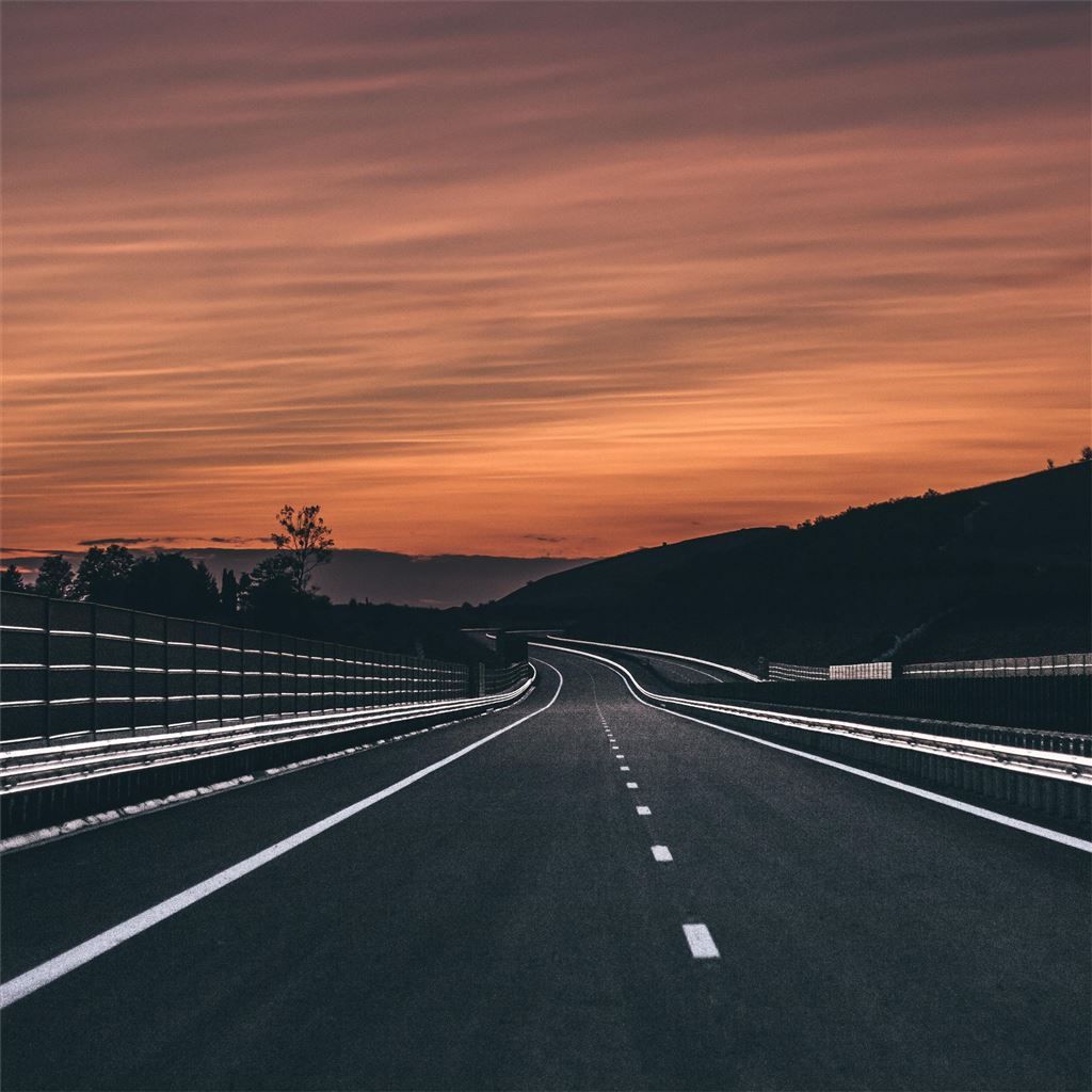 A highway at sunset with the sky painted in orange and pink hues - Road