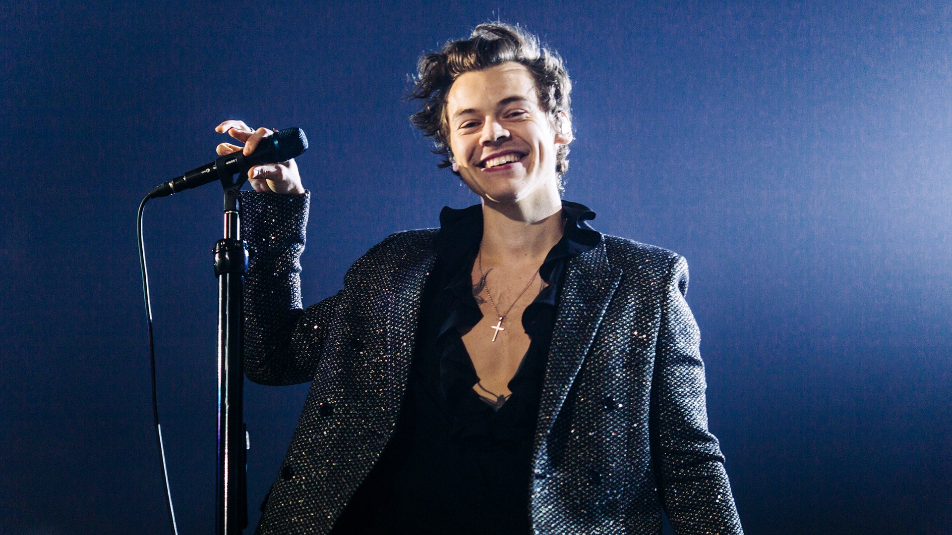 A man in black suit and shirt holding microphone - Harry Styles