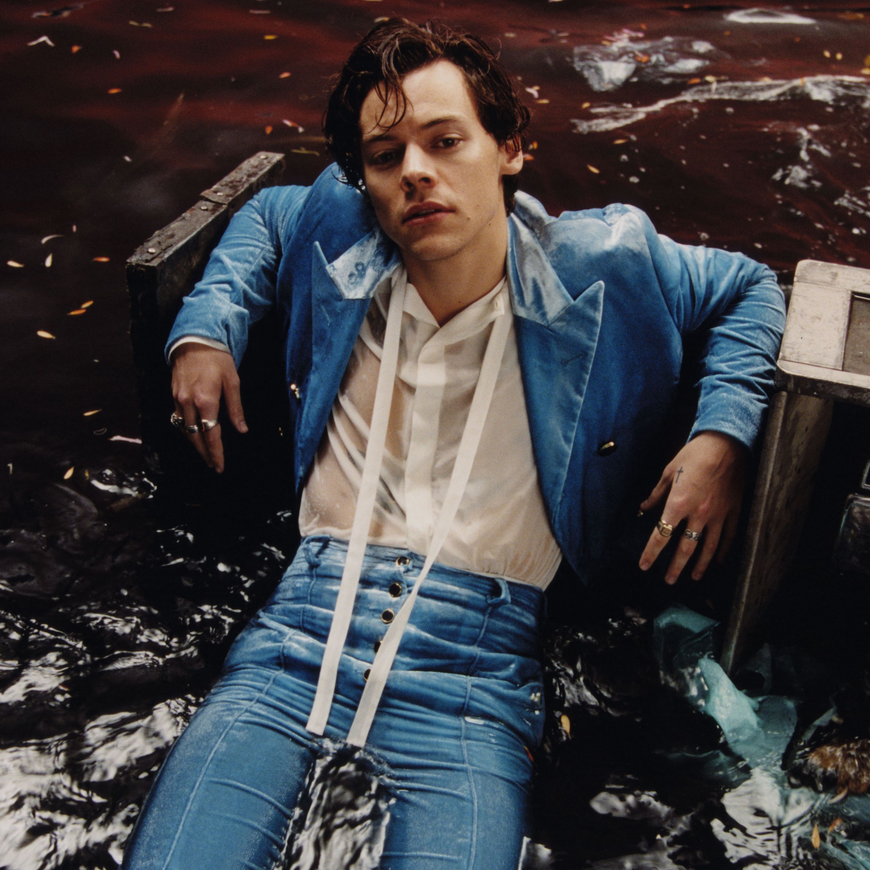 A man in blue pants and jacket laying on the ground - Harry Styles