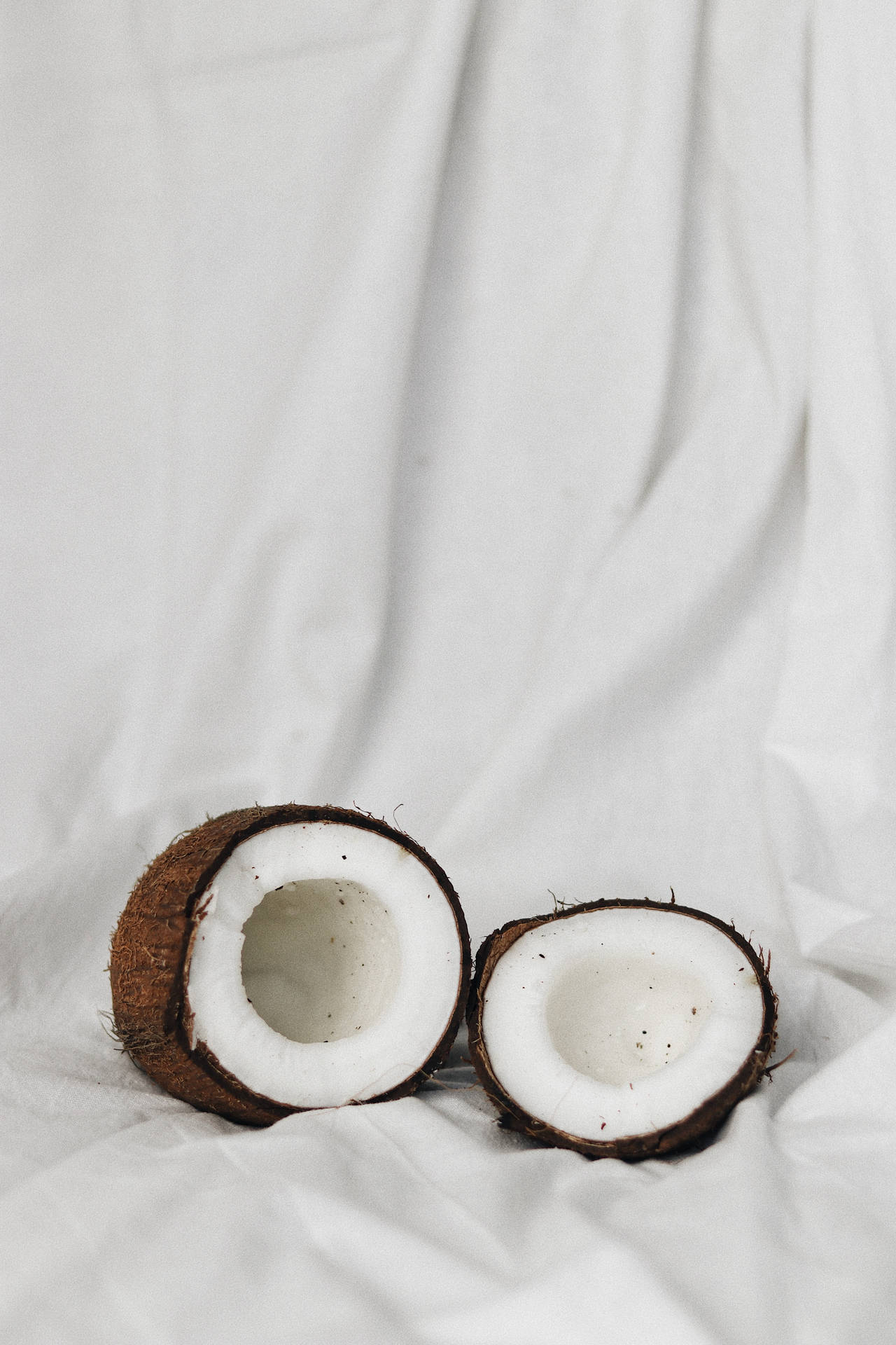 A coconut cut in half on a white sheet. - Coconut