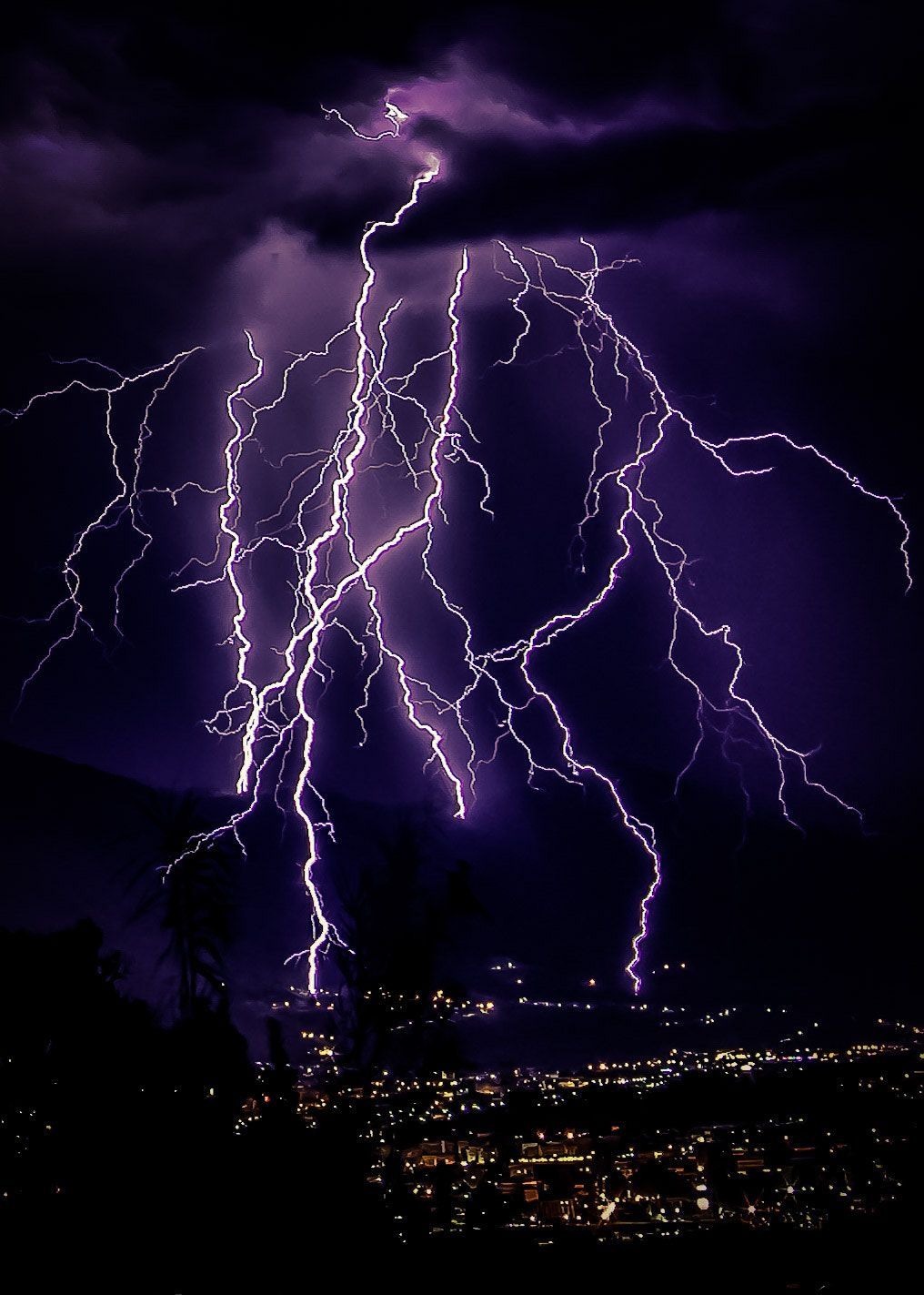 Lightning strikes in the sky over a city at night. - Lightning