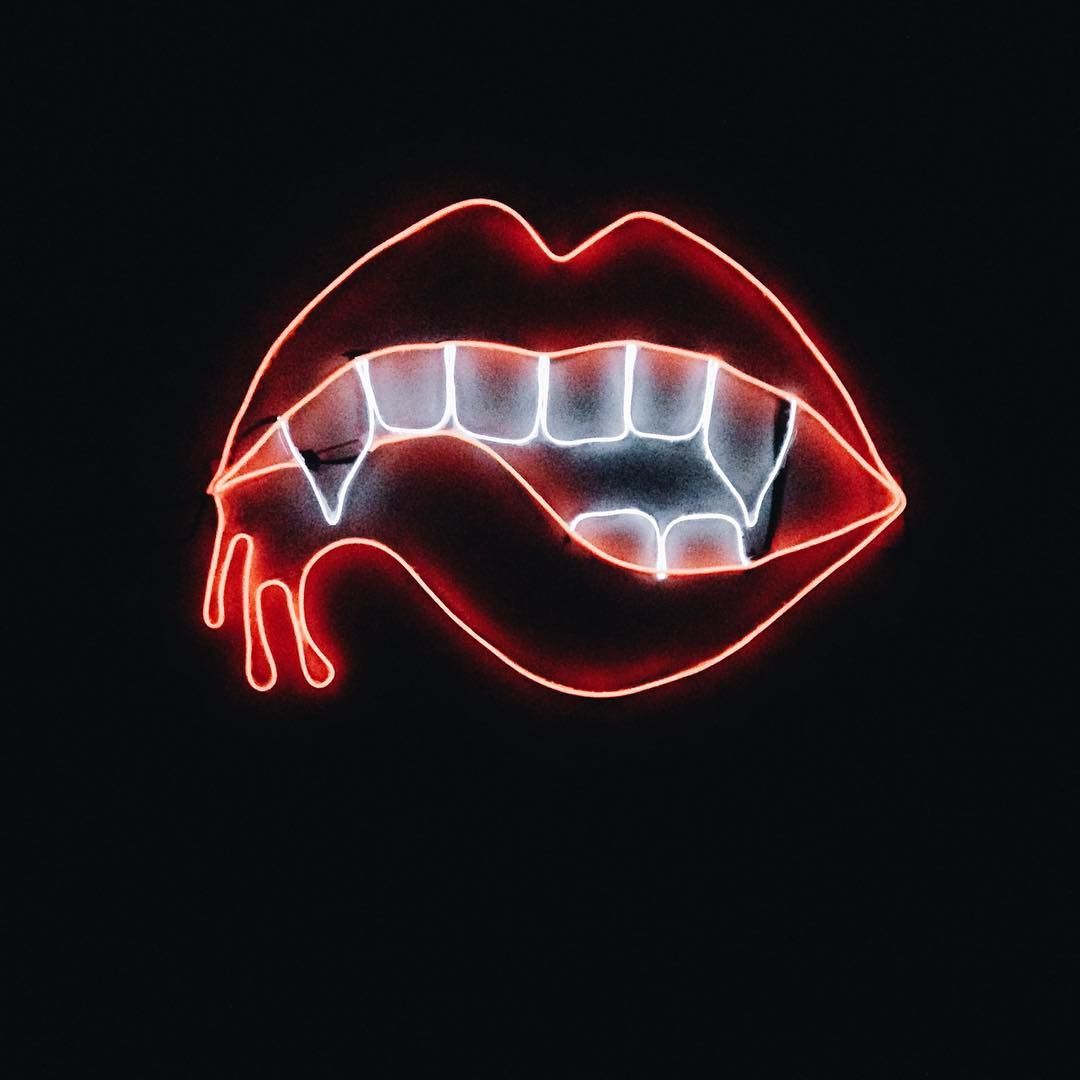 A neon sign of a mouth with red lips and white teeth. - Vampire