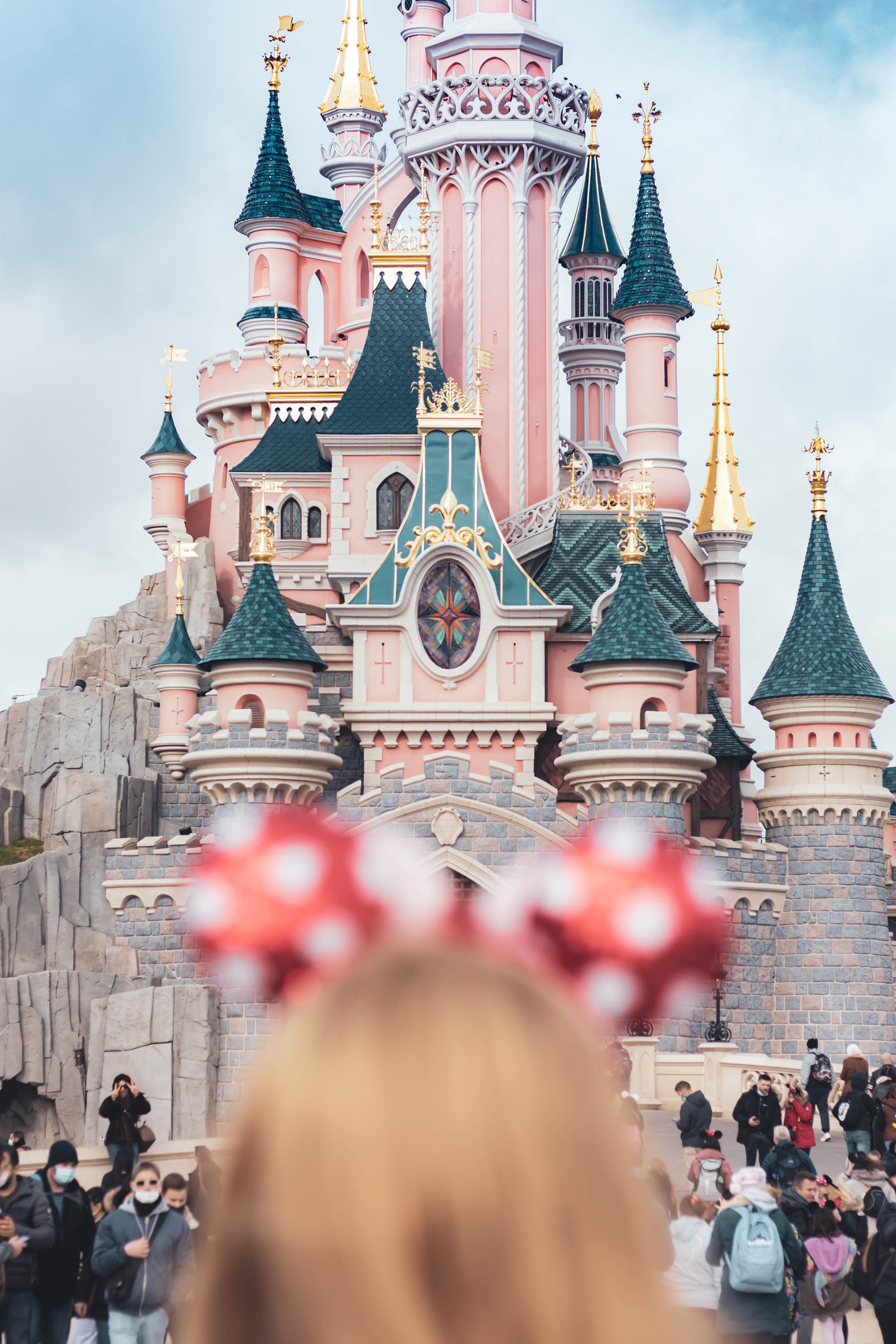 A woman with a Minnie Mouse ear headband in front of a pink castle. - Disneyland