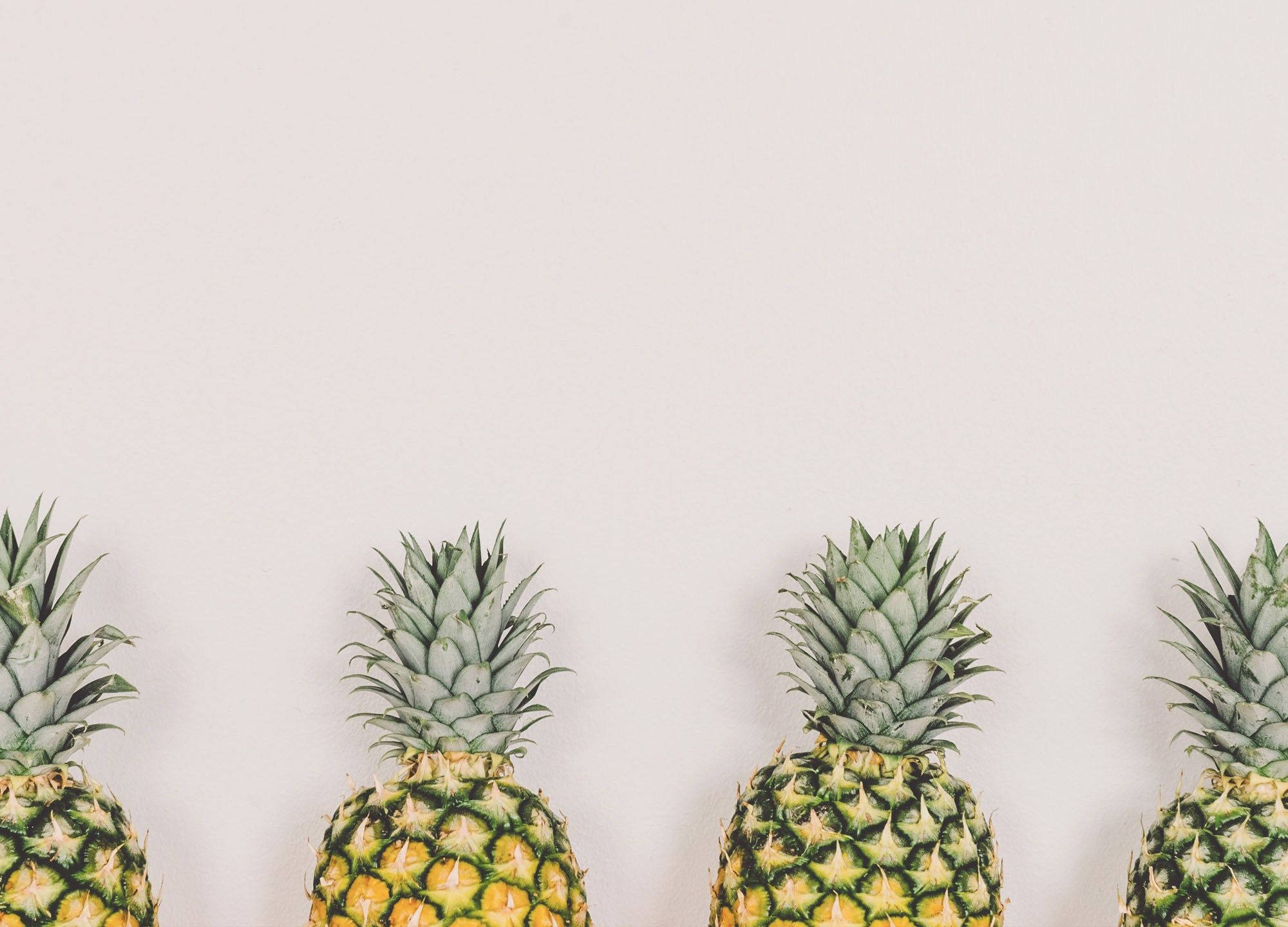 Four pineapples lined up in a row against a white background - Pineapple