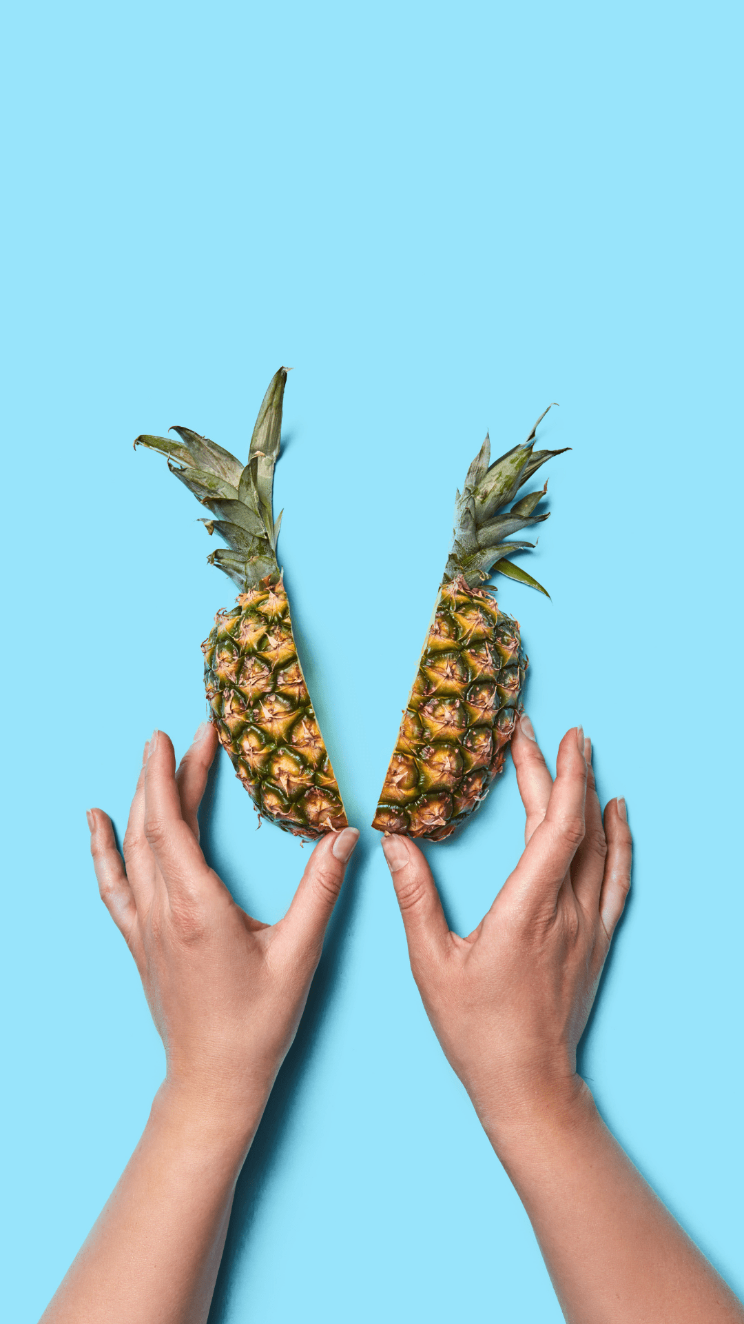 A woman's hands holding a pineapple cut in half on a blue background - Pineapple, summer