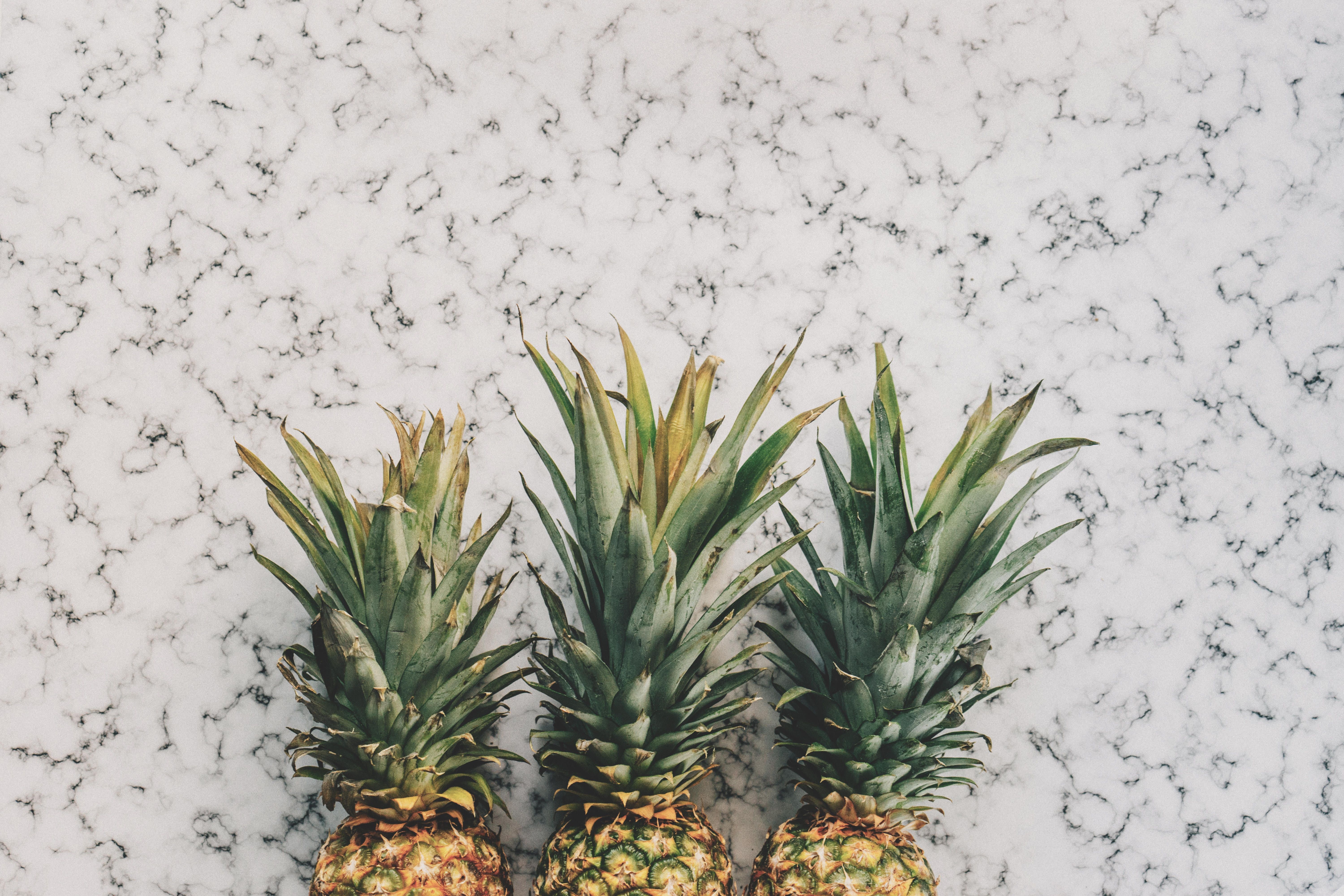 Three pineapples lined up on a marble counter. - Pineapple