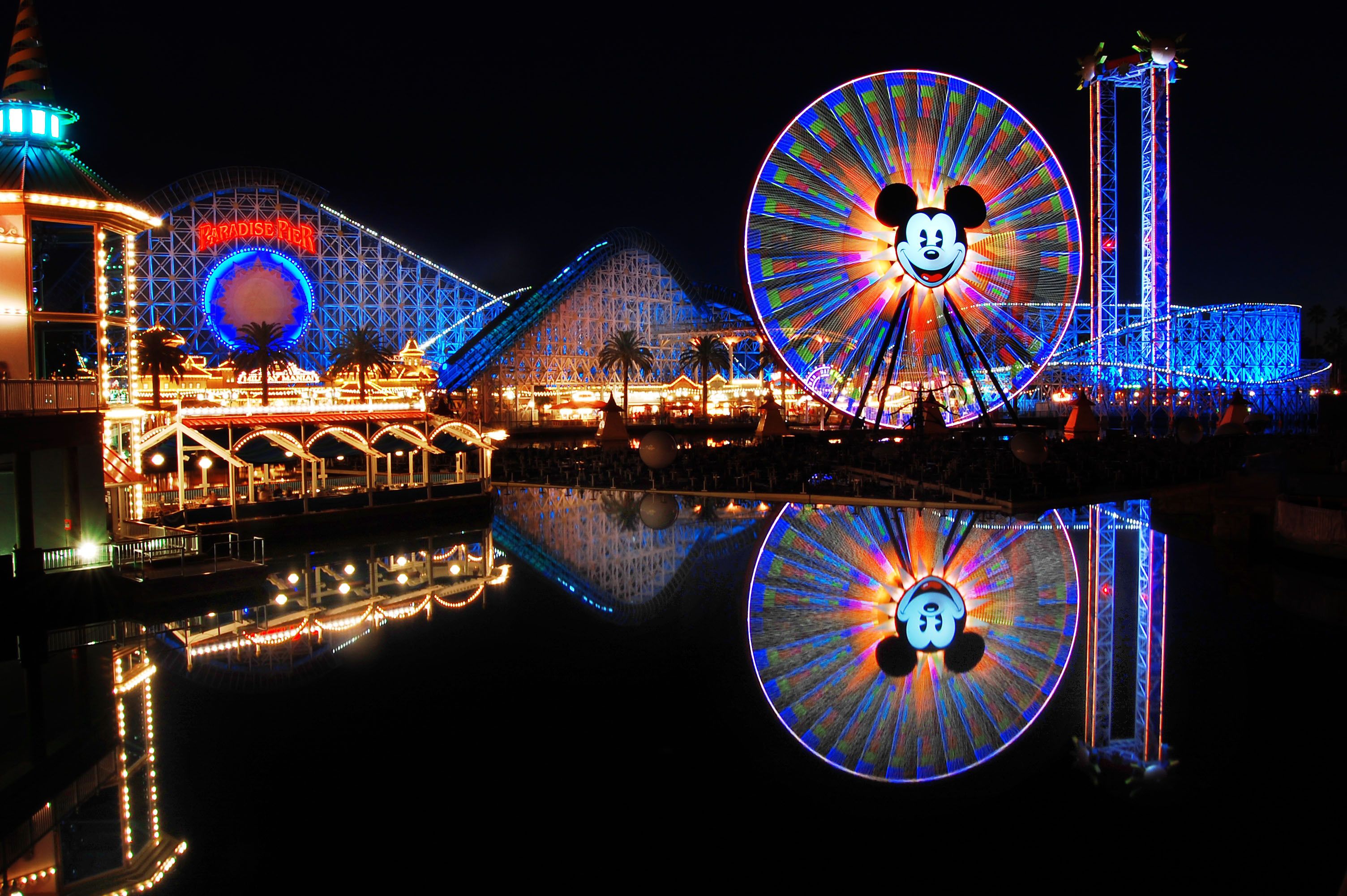 A colorful lit up roller coaster and ferris wheel at night. - Disneyland