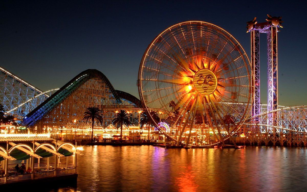 A large ferris wheel at night in front of water - Disneyland