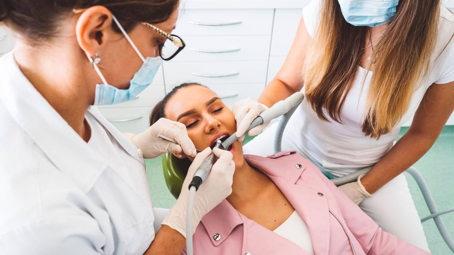 A woman having her teeth cleaned by a dentist and hygienist. - Dentist