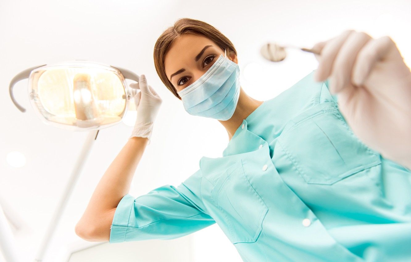 A dental hygienist in blue scrubs holding a dental tool - Dentist