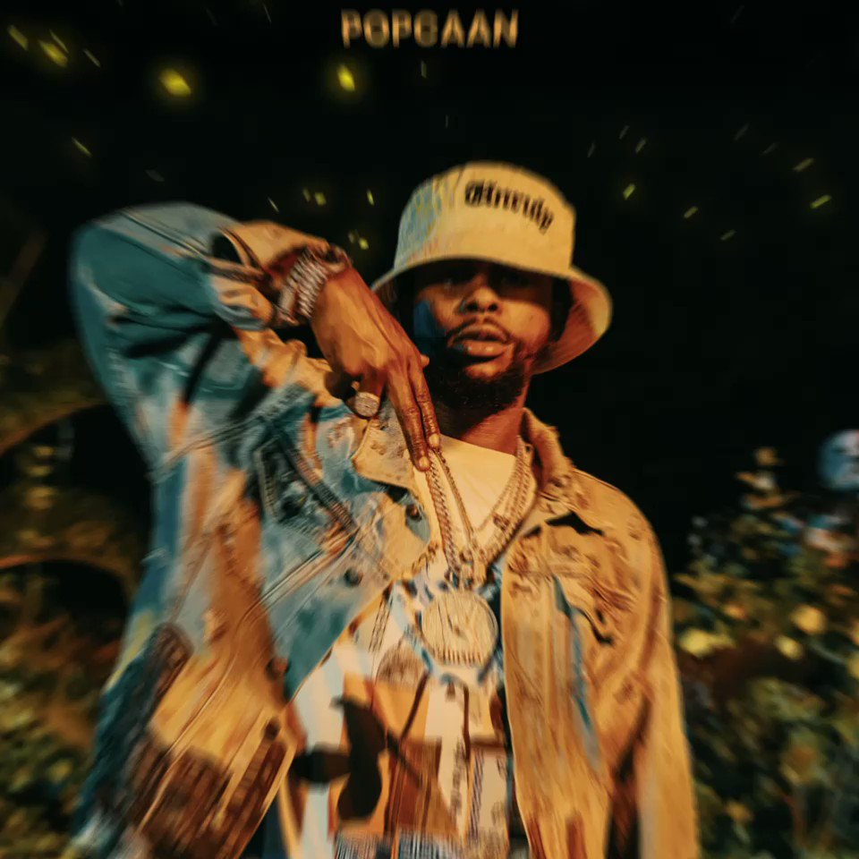 Popcaan wearing a hat and jacket in front of a black background - Pop Smoke