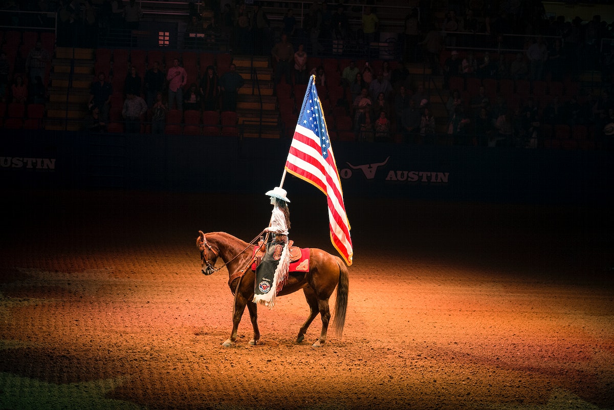 A person on a horse holding a flag. - Western