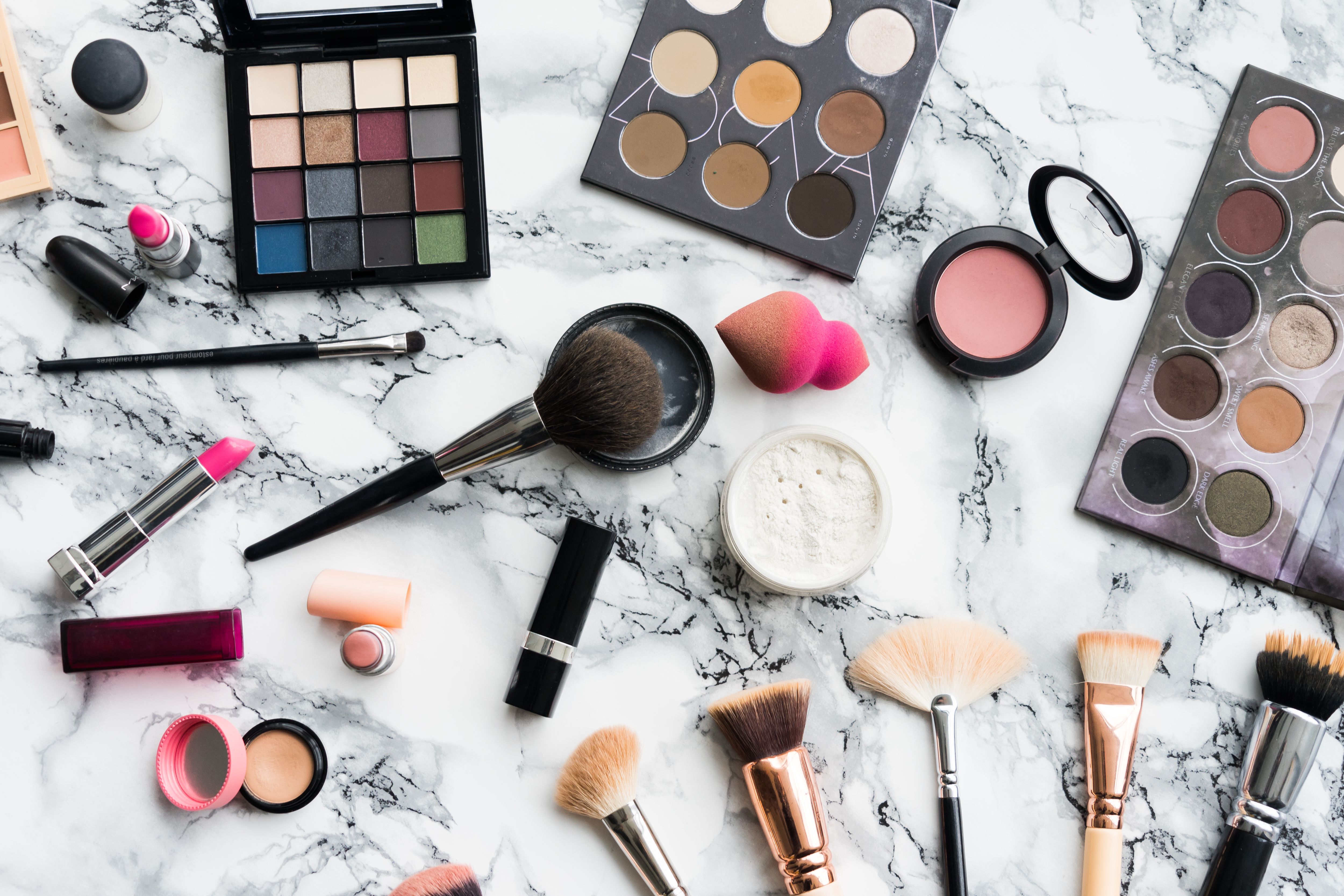 Various makeup products such as foundation, eye shadow, lipstick, and brushes on a marble surface. - Makeup
