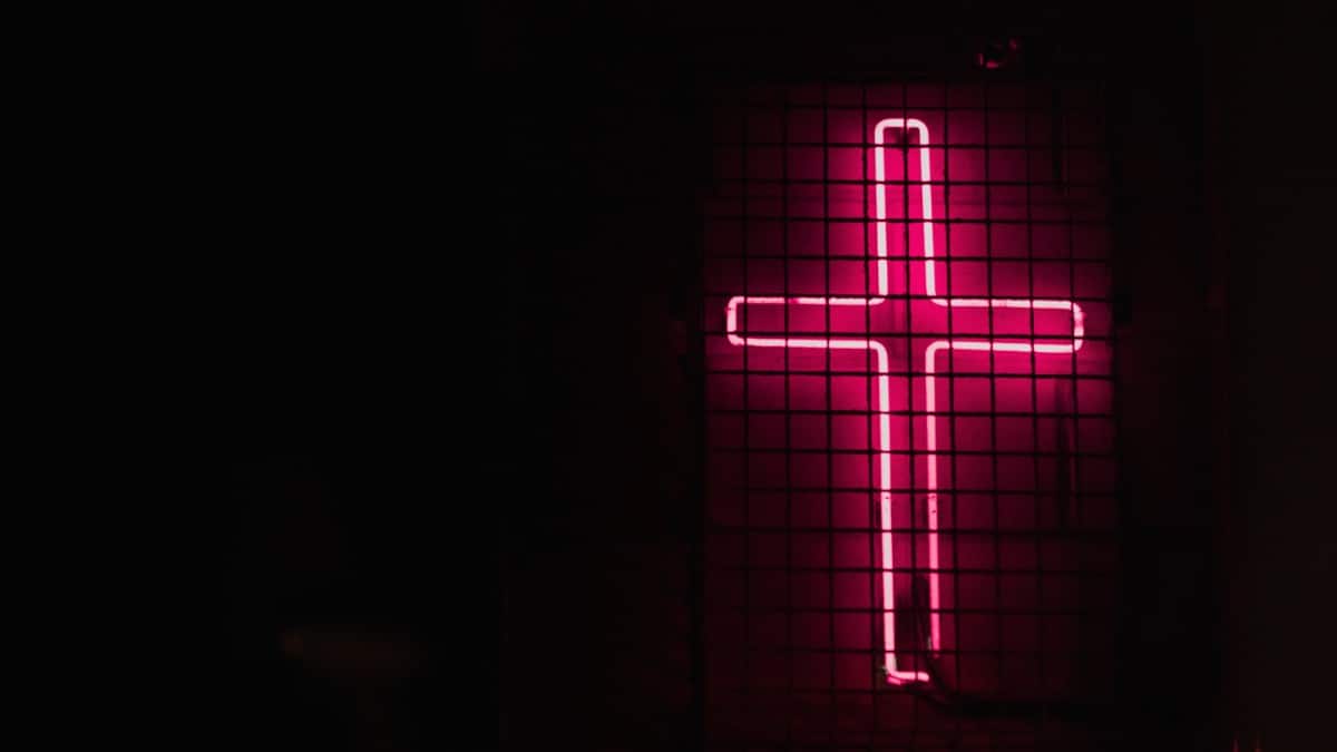 A pink neon cross on a black background. - Christian