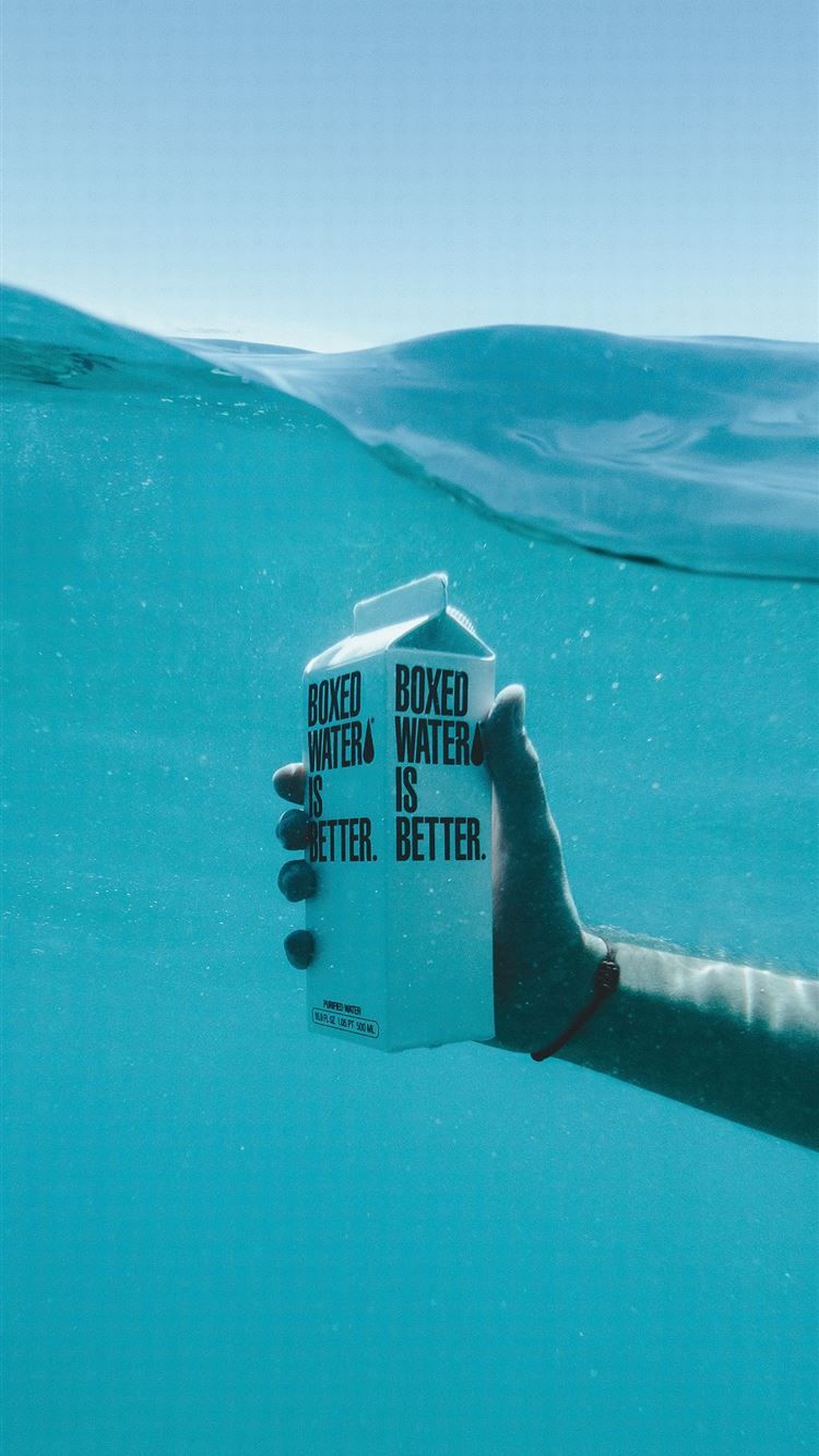 A person's hand holding a carton of Boxed Water in the ocean - Underwater