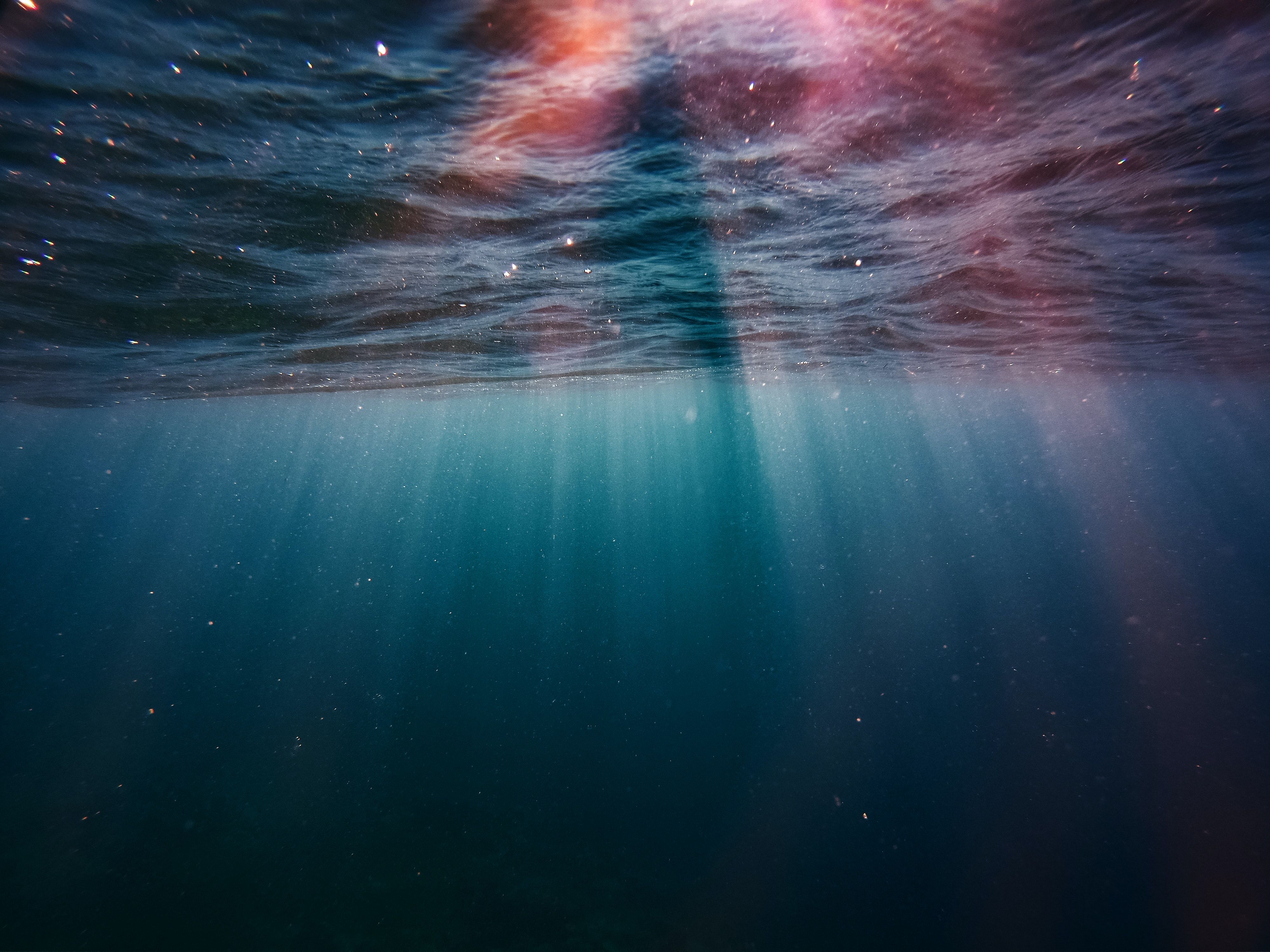 A person swimming underwater with sunlight shining through the water's surface - Underwater