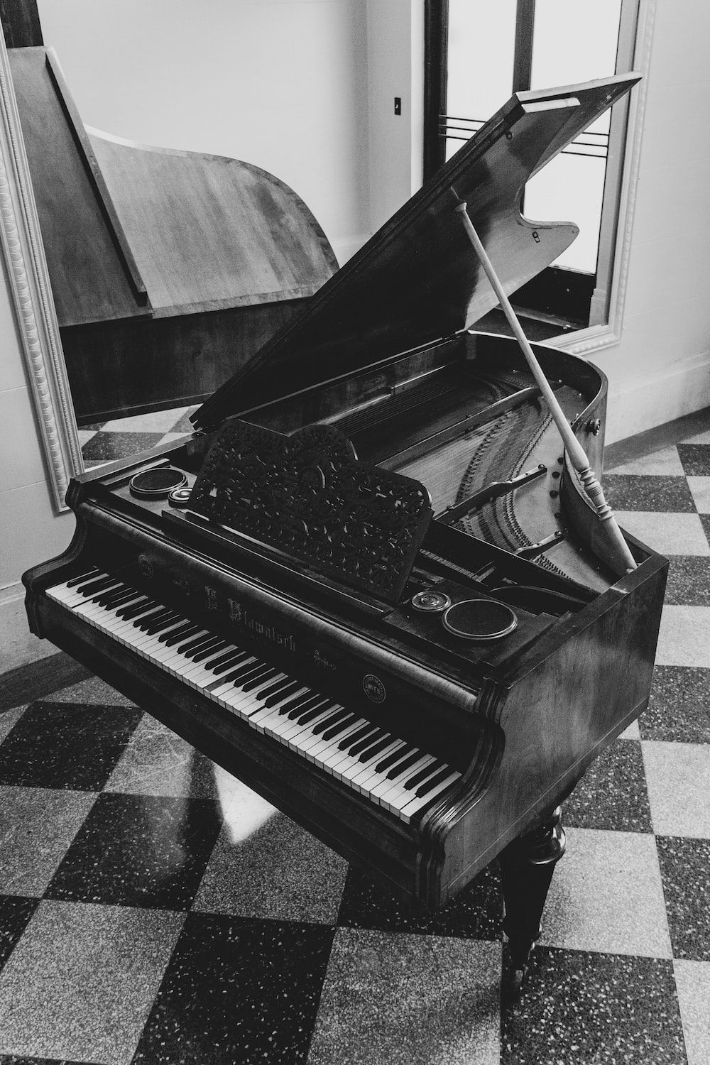 A black and white photo of a piano with the lid open and a baton resting on it. - Piano