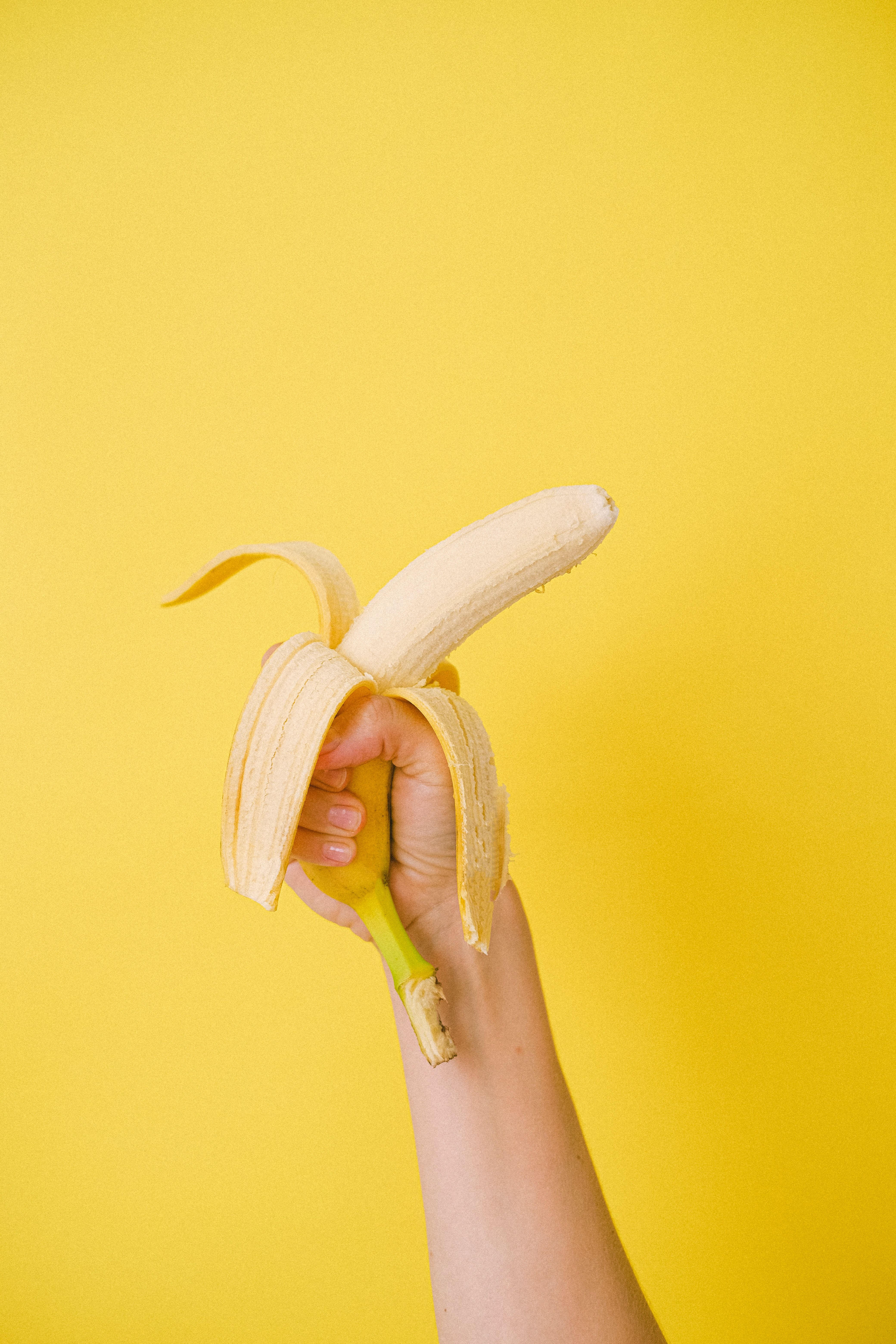 A hand holding up half of an unpeeled banana - Banana