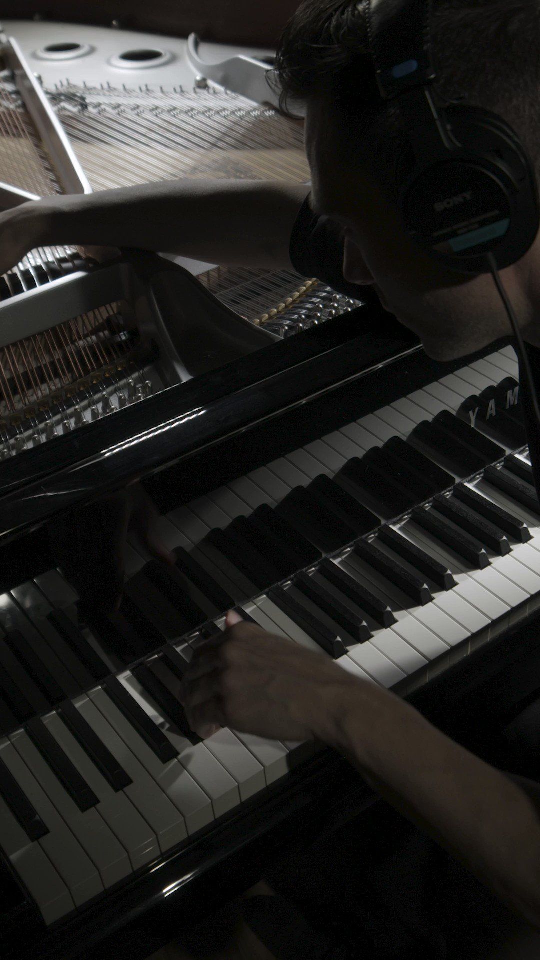 A man wearing headphones playing a piano. - Piano