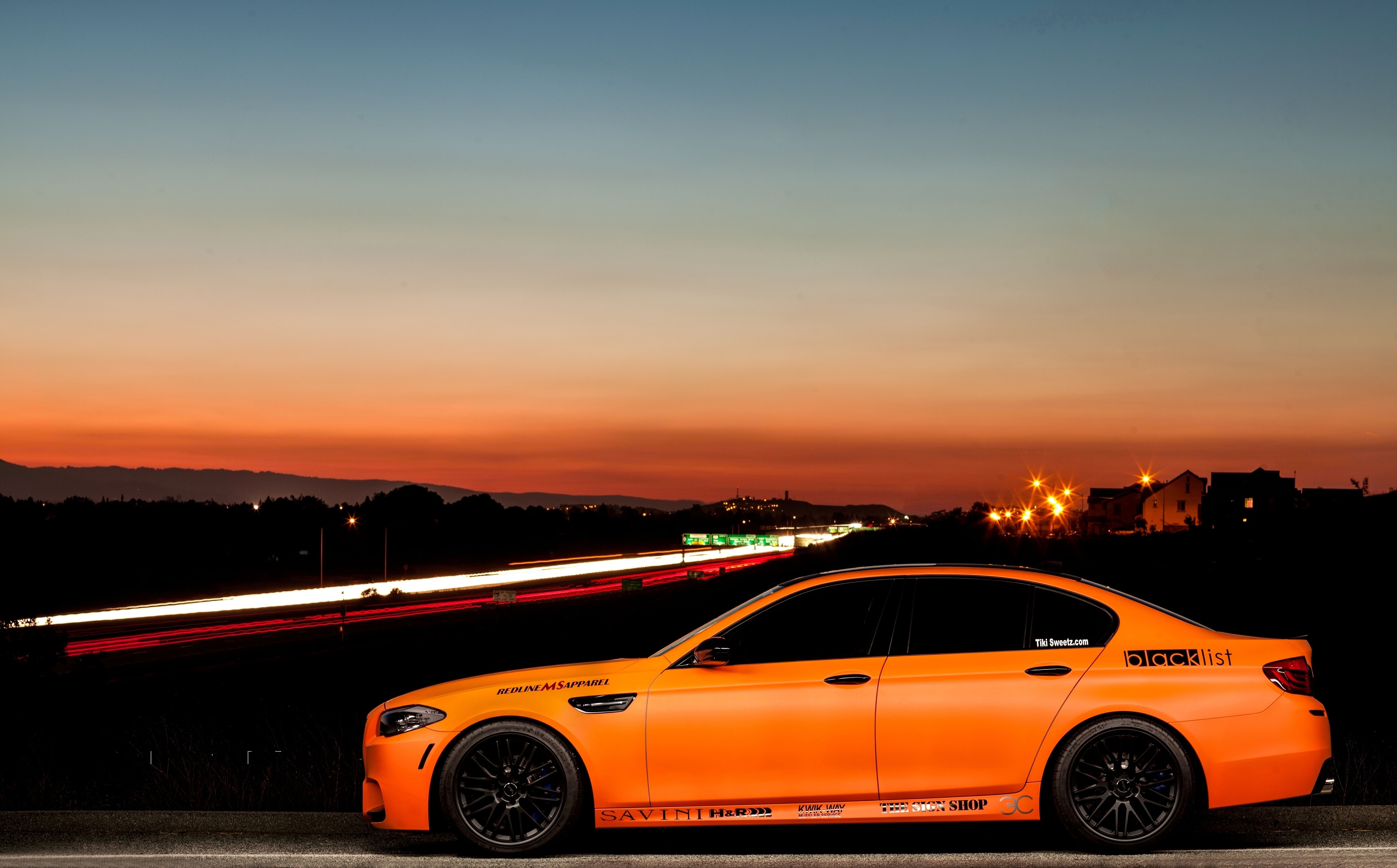 An orange BMW M5 stands on the road at sunset. - BMW