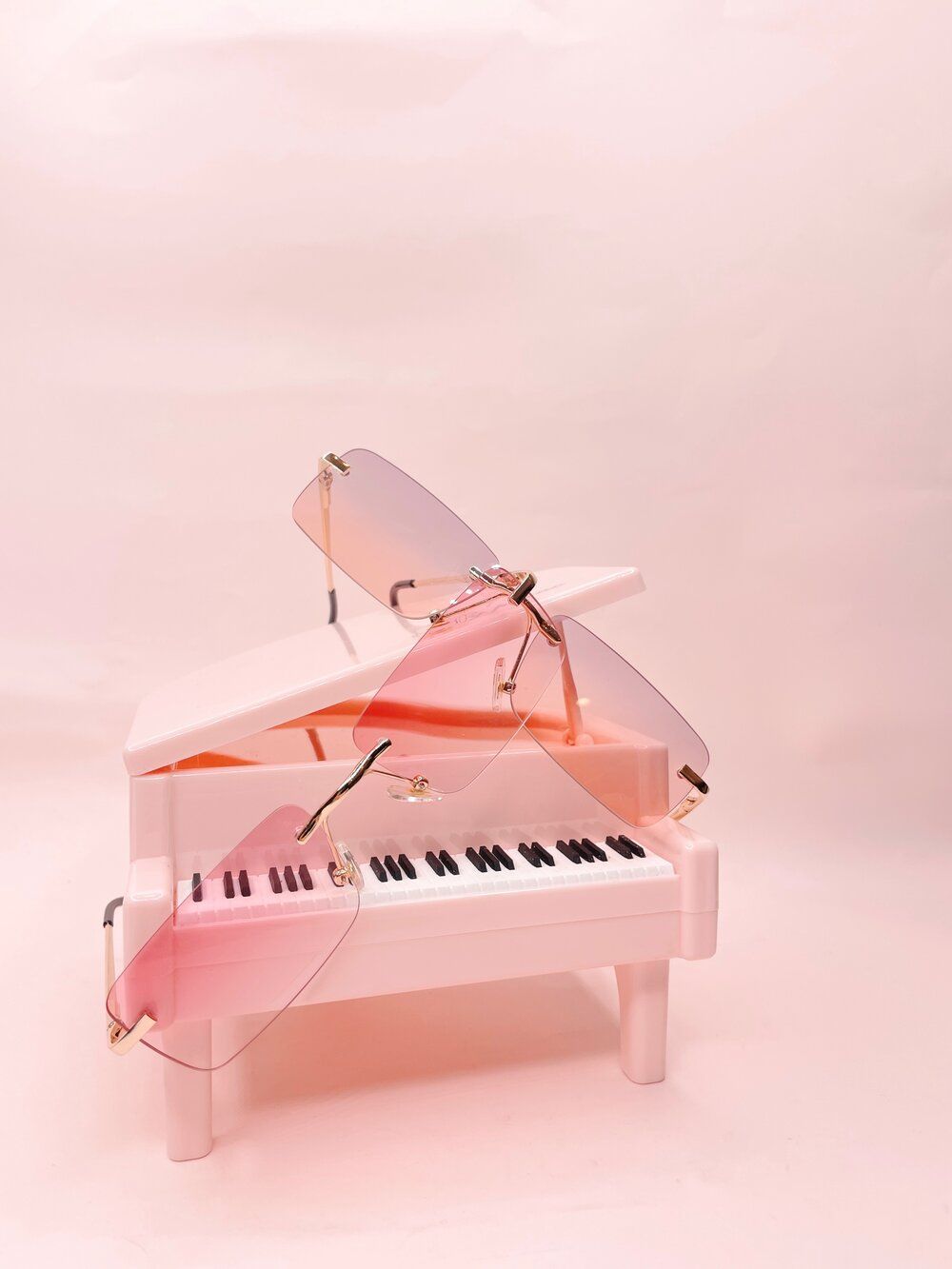 A pair of pink sunglasses sitting on top of a pink piano. - Piano