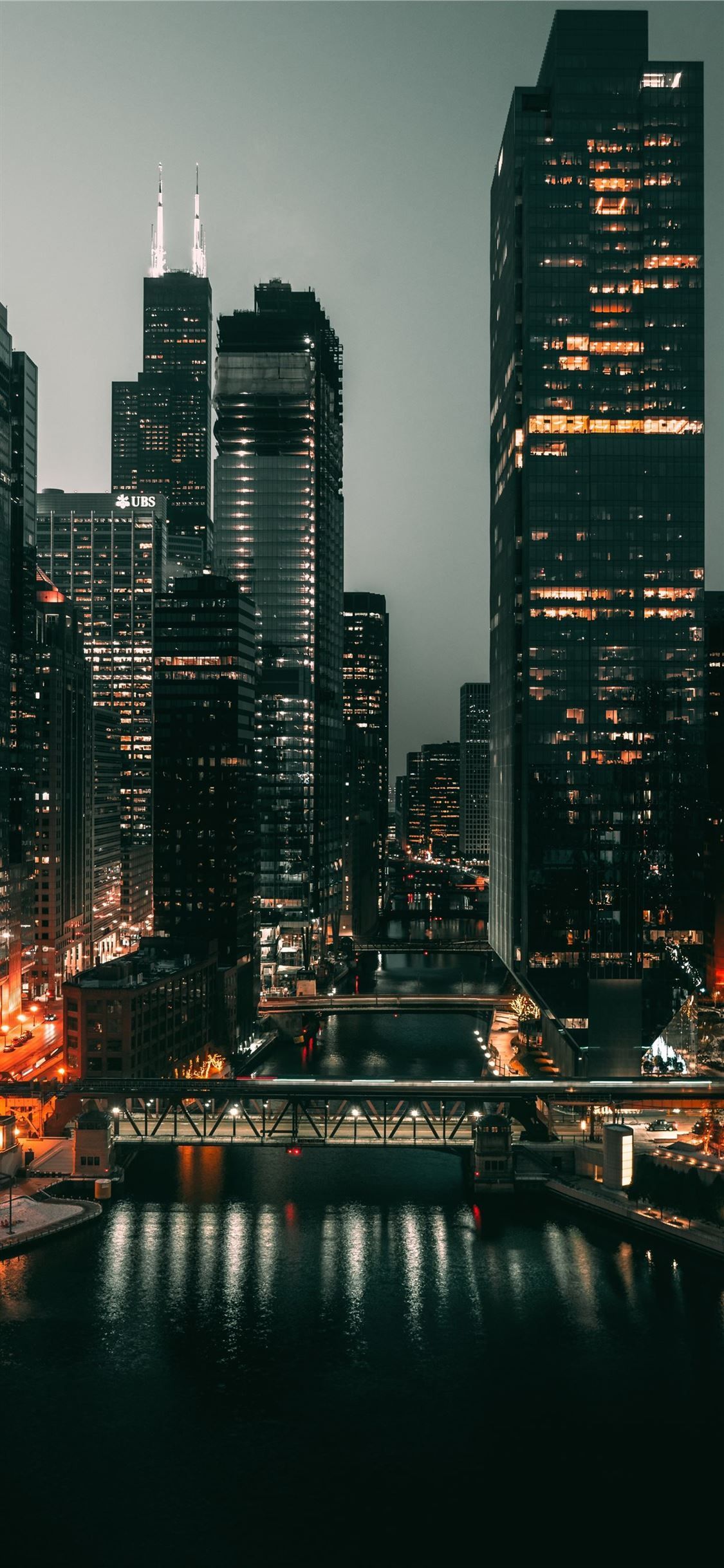 A night time cityscape of Chicago, with the river in the foreground and the city lights illuminating the buildings. - Chicago