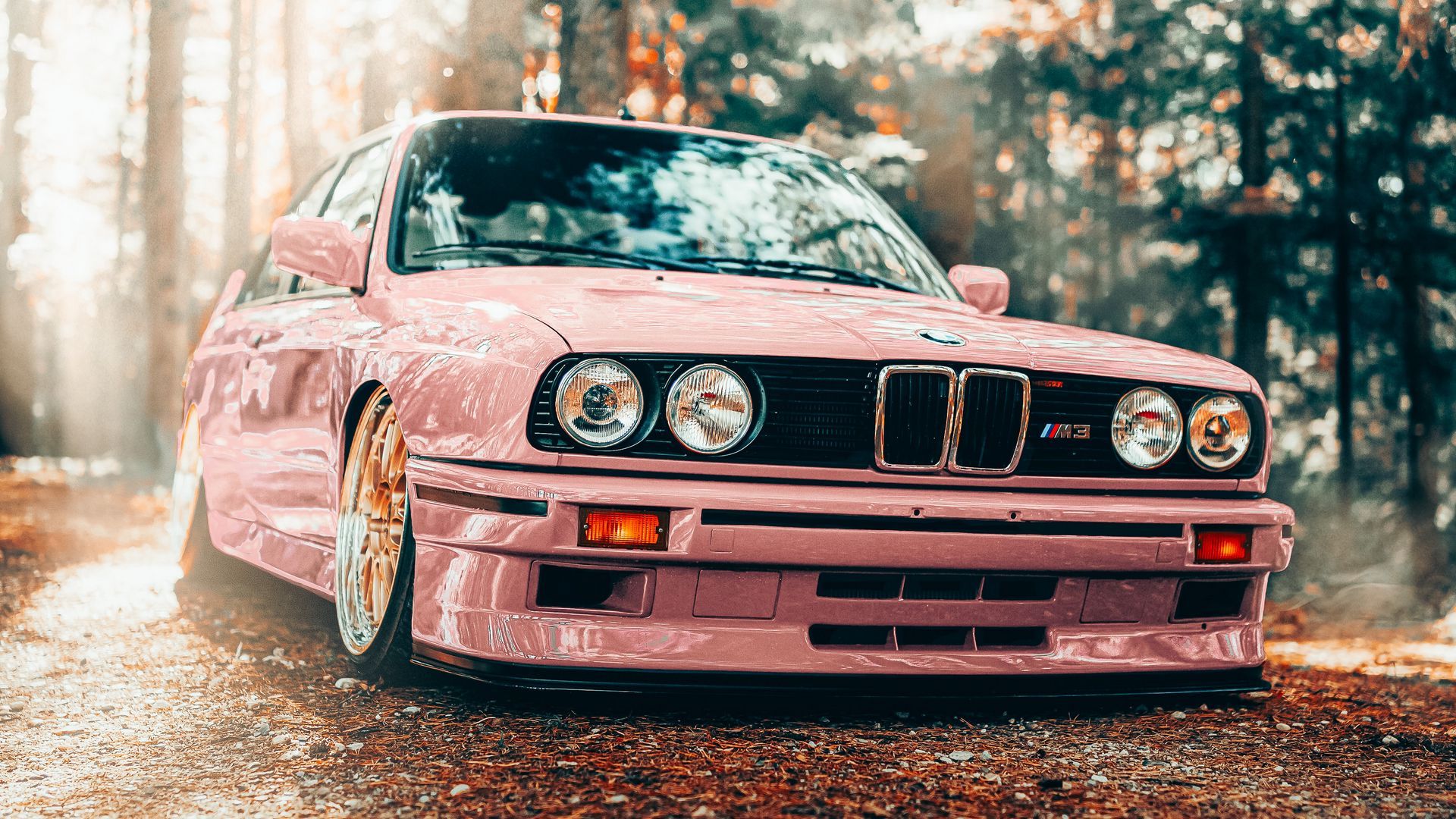 A pink BMW E30 with gold wheels parked in a forest - BMW