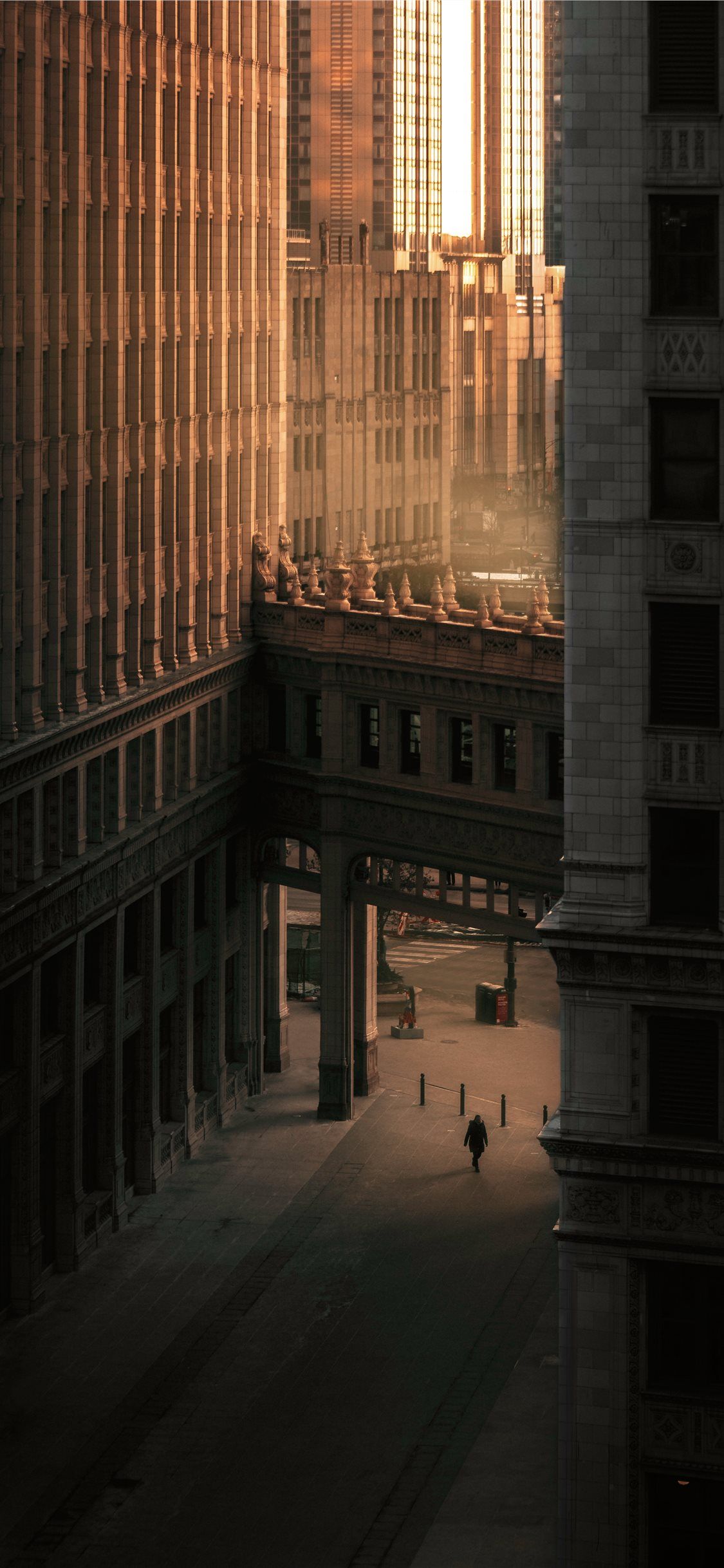 IPhone wallpaper of a person walking down a street with tall buildings on either side. - Chicago