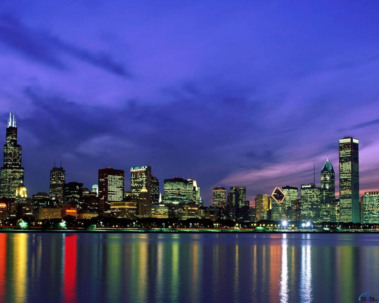 A city skyline at night with the water reflecting it - Chicago