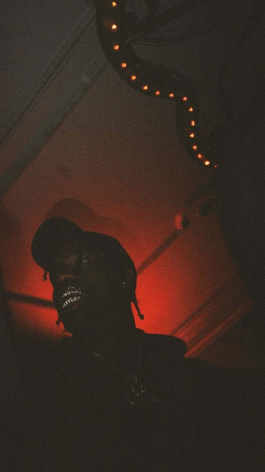 A man with a face mask and a black hoodie in a dark room with red light - Travis Scott
