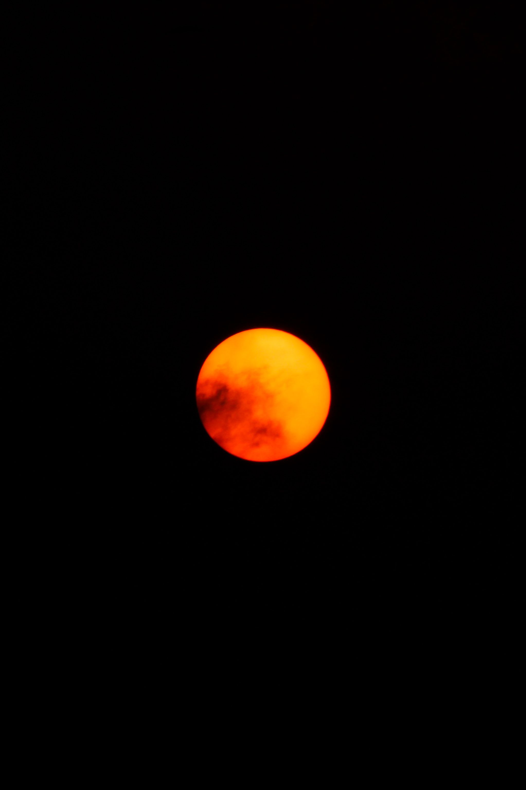 A red sun setting behind a black sky. - Dark orange