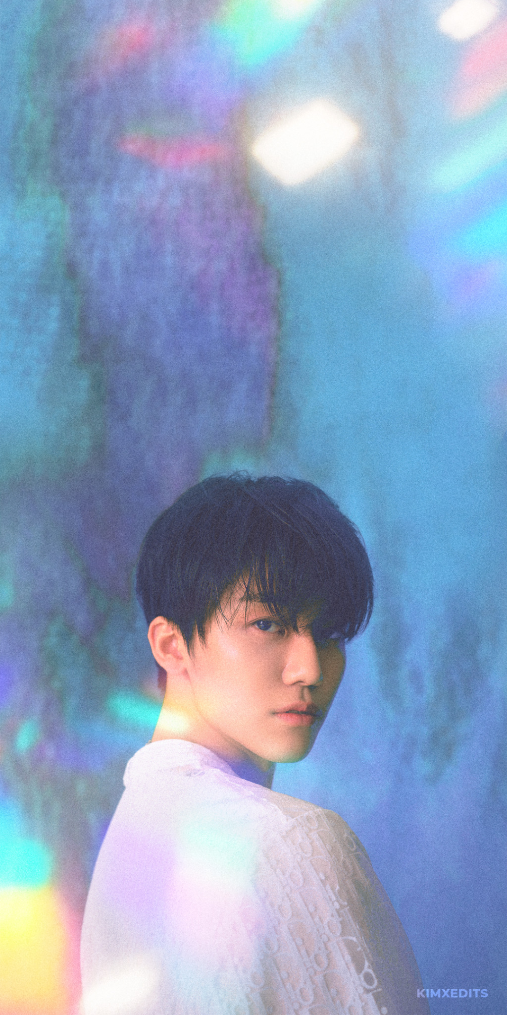 A young man with black hair and bangs, wearing a white shirt, stands in front of a rainbow background. - NCT