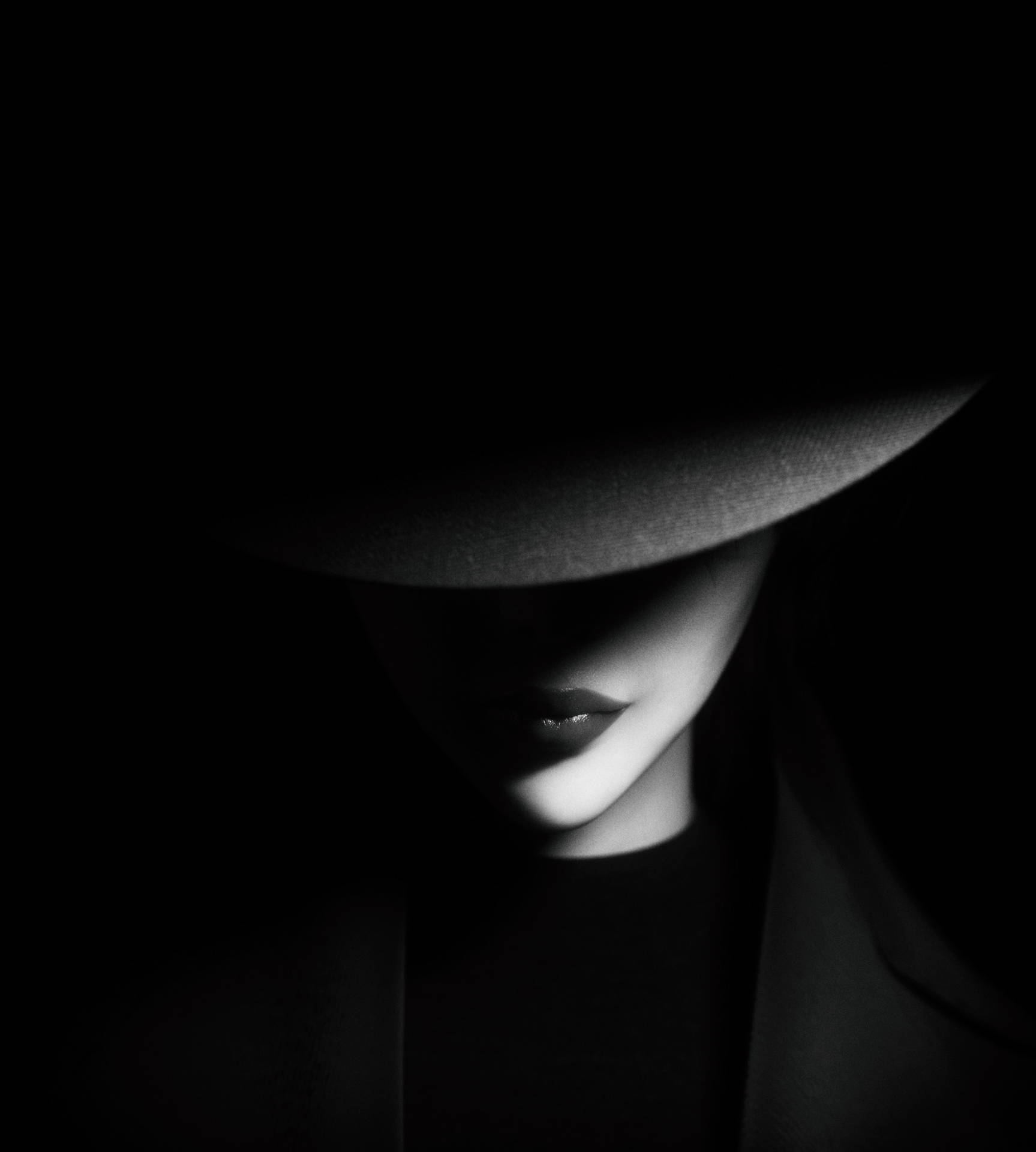 A woman in black with her face obscured by the hat - Shadow