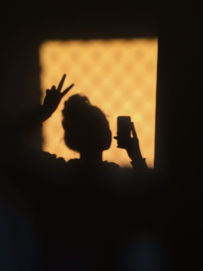 A person's silhouette holding a phone up to take a photo. - Shadow