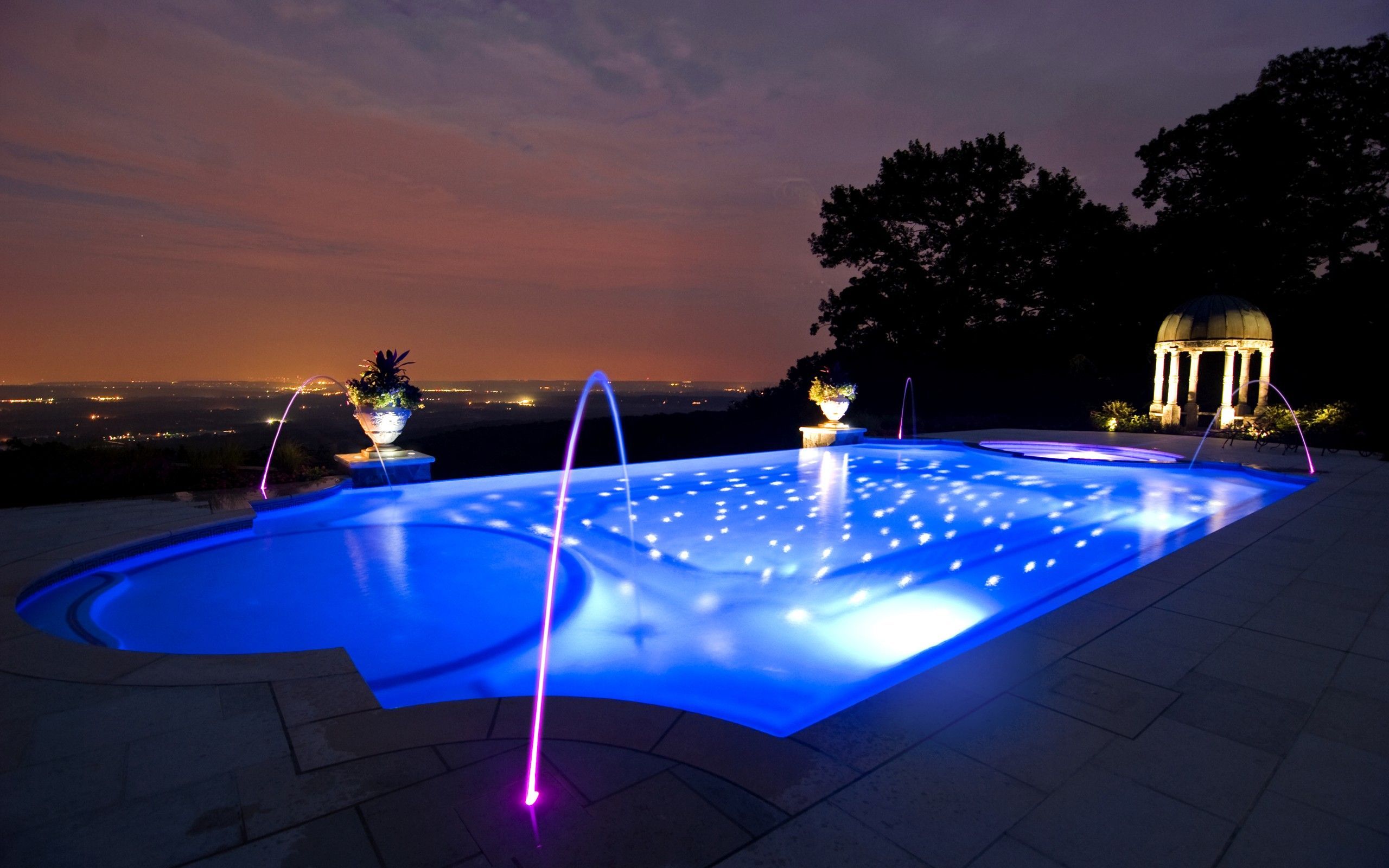 A pool with water features lit up at night - Swimming pool