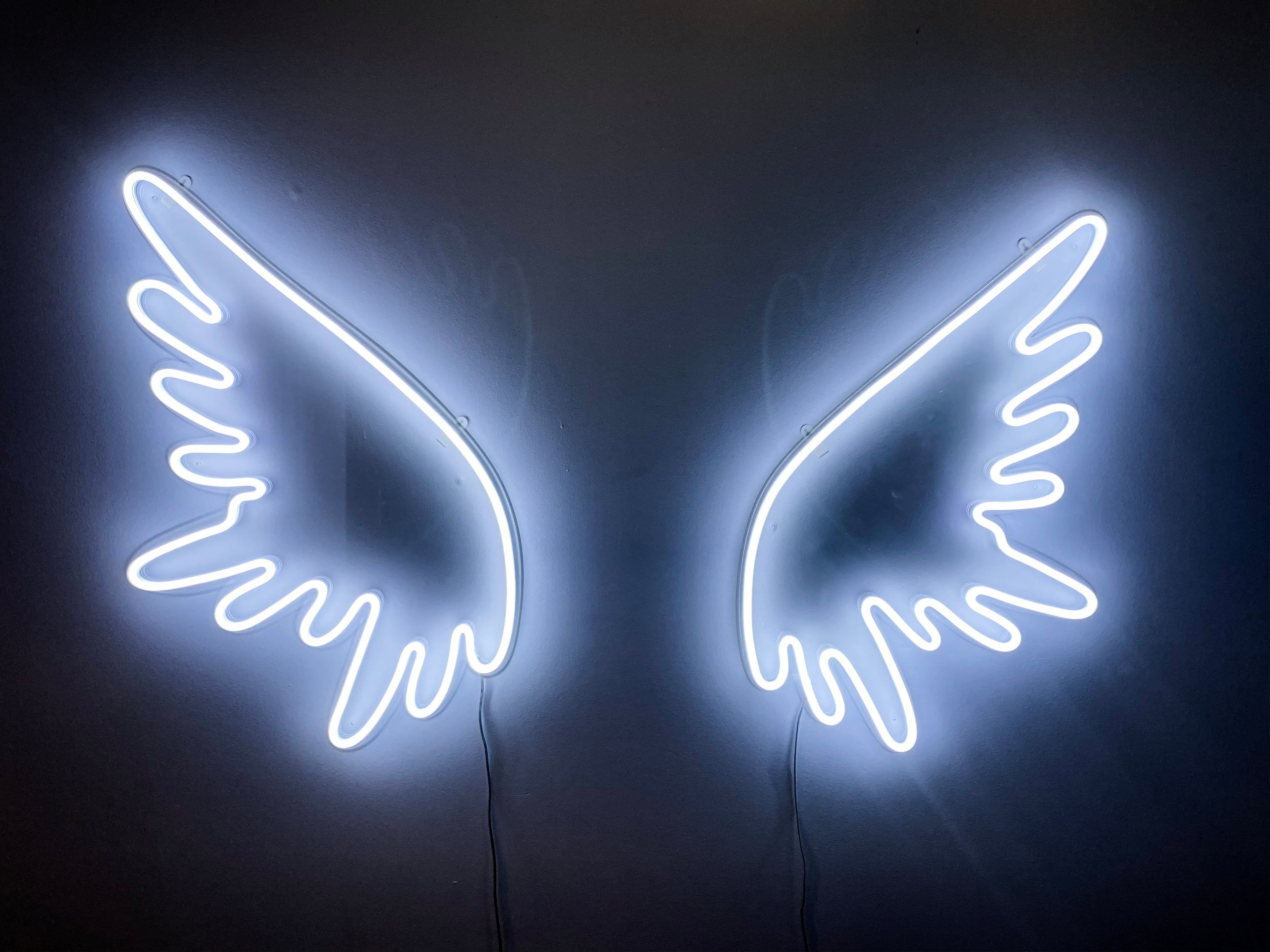 A pair of white neon wings on a black wall. - Wings