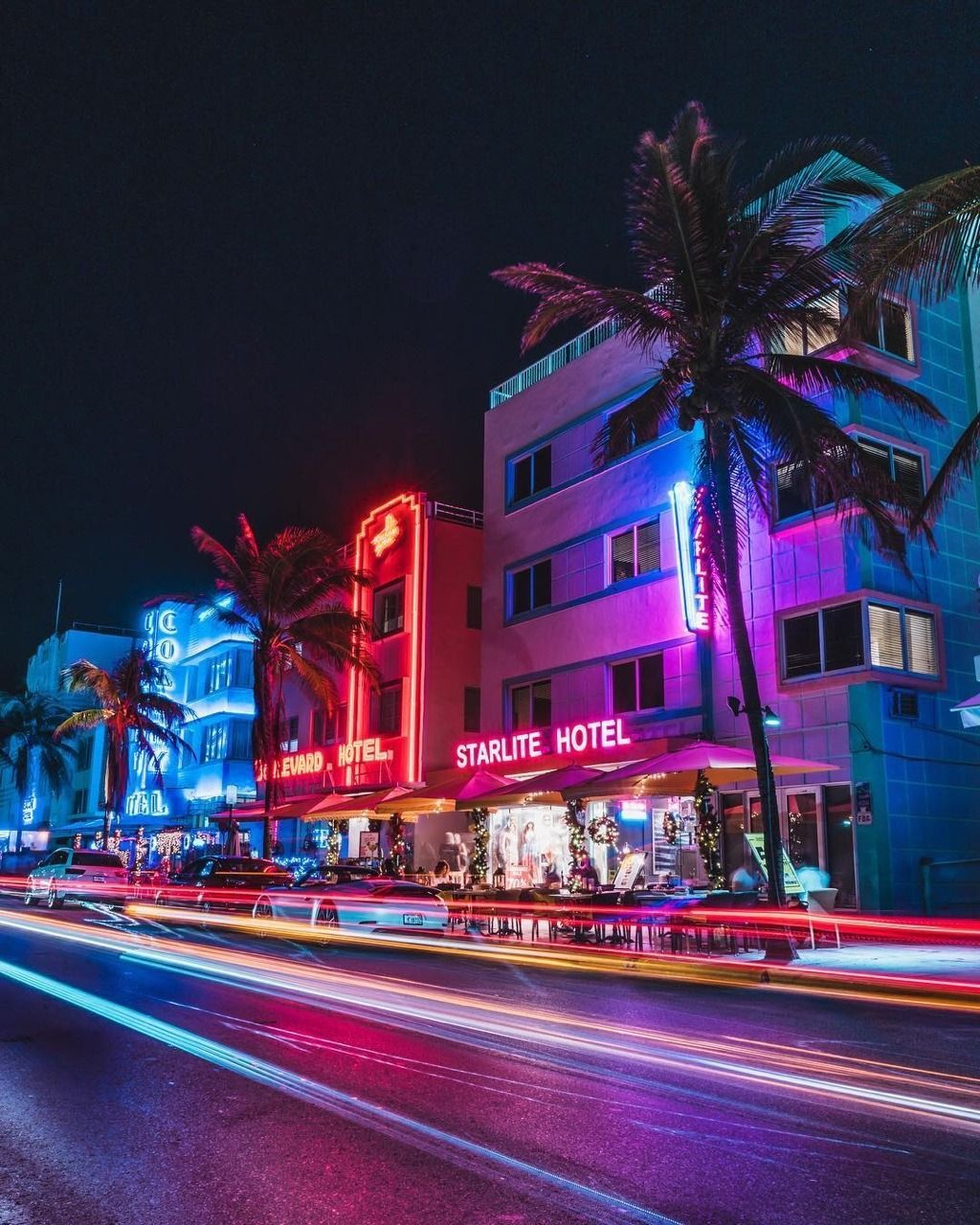 A city street with neon lights and palm trees - Miami