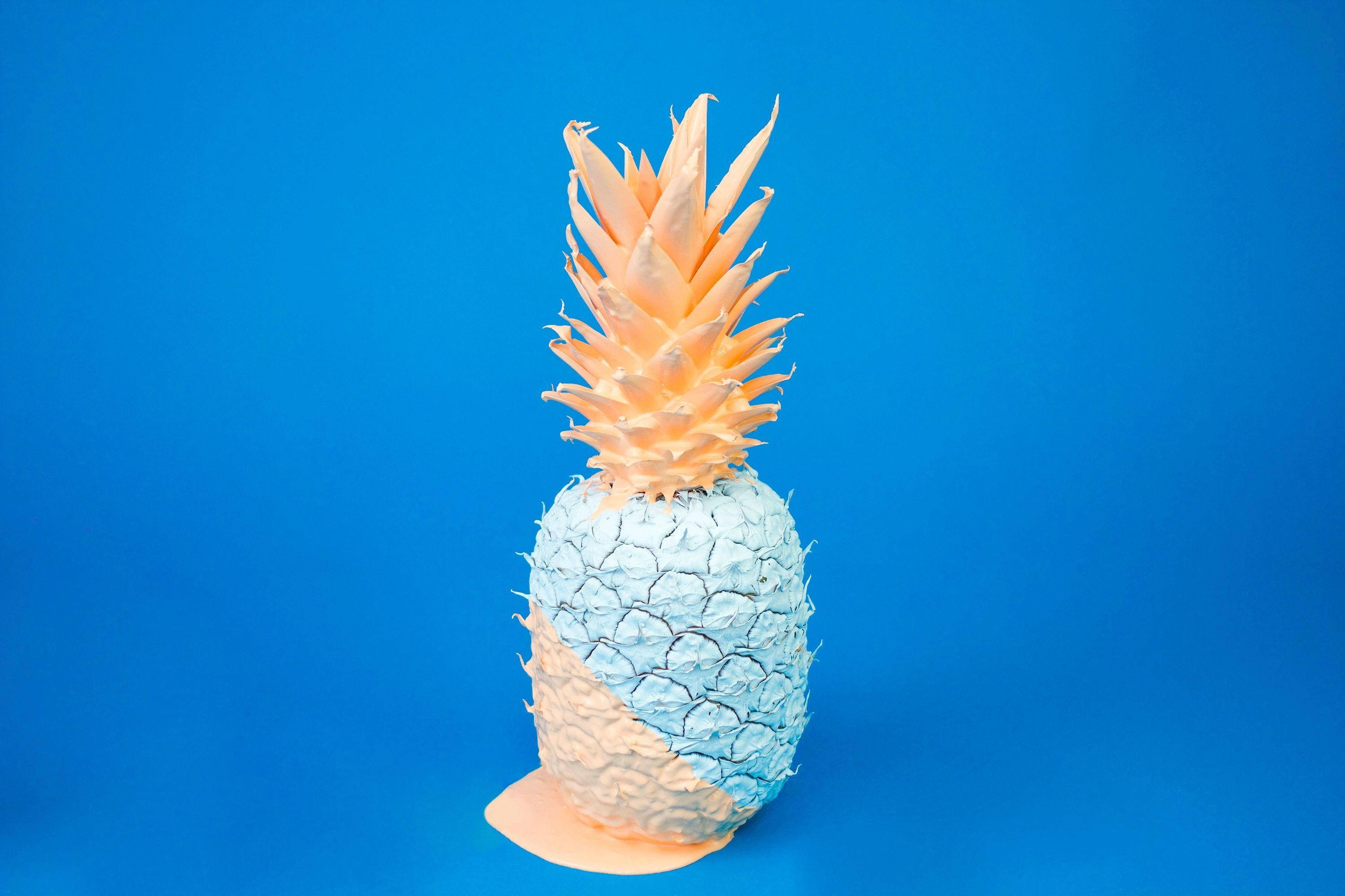 A pineapple painted in pastel blue and pink sits on a blue background. - Pineapple