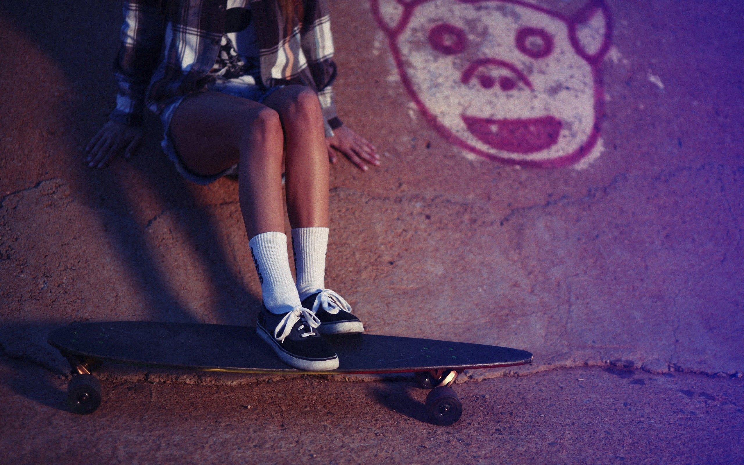 A person sitting on a skateboard with a monkey face painted on the wall behind them. - Skater
