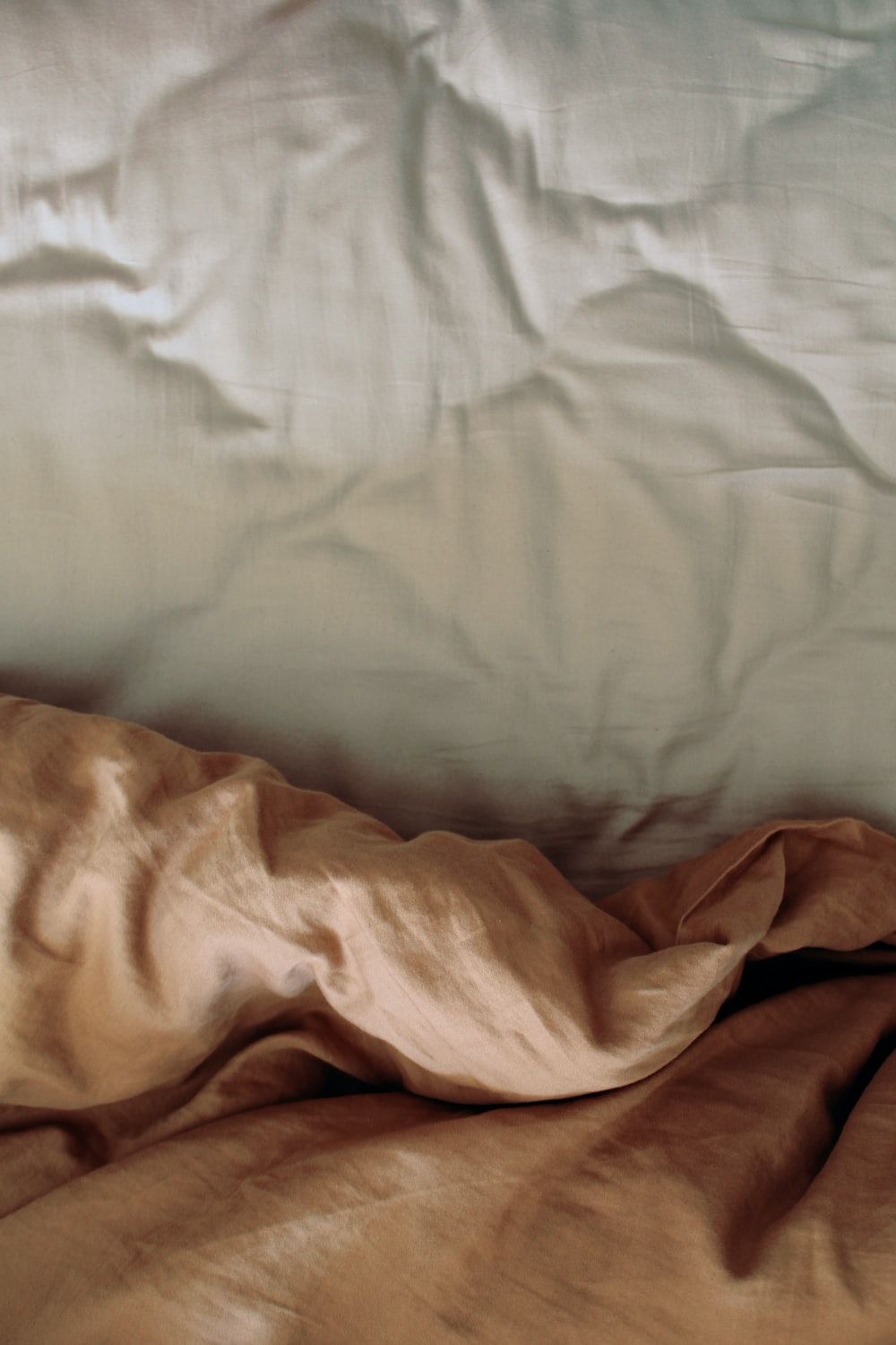 An unmade bed with white and brown sheets. - Neutral