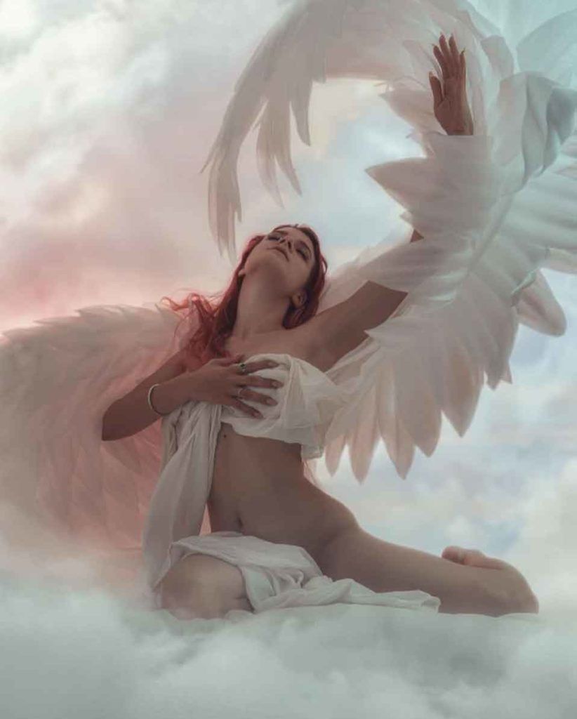 A woman dressed as an angel sitting on clouds - Angelcore