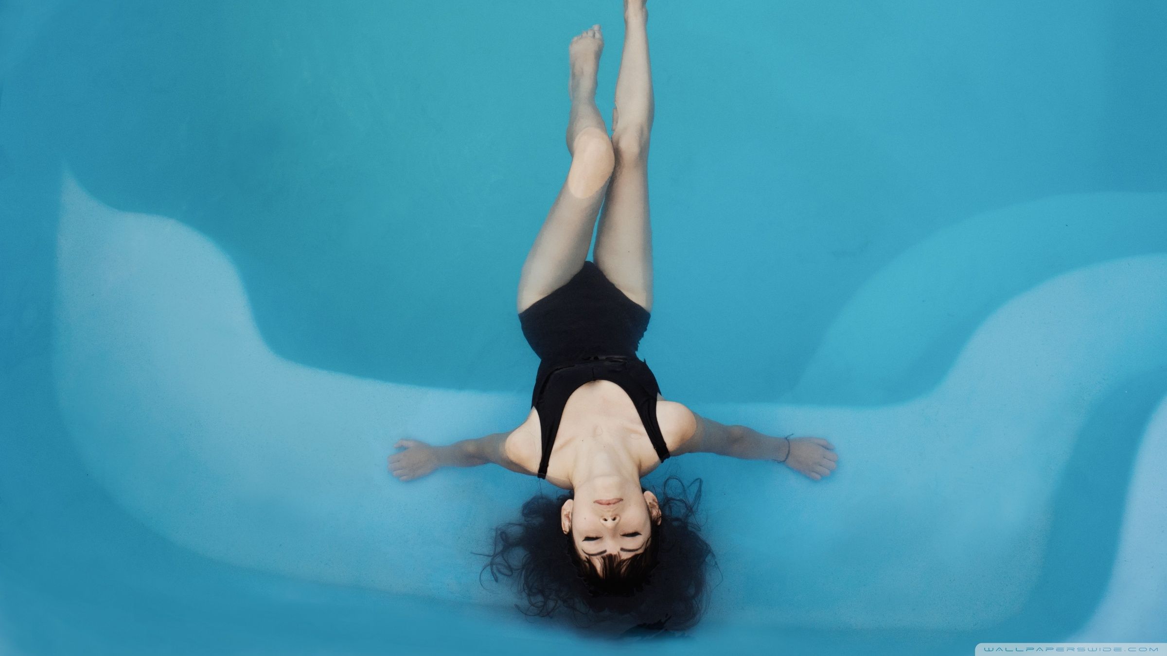 A woman in a black swimsuit floating in a blue pool - Swimming pool